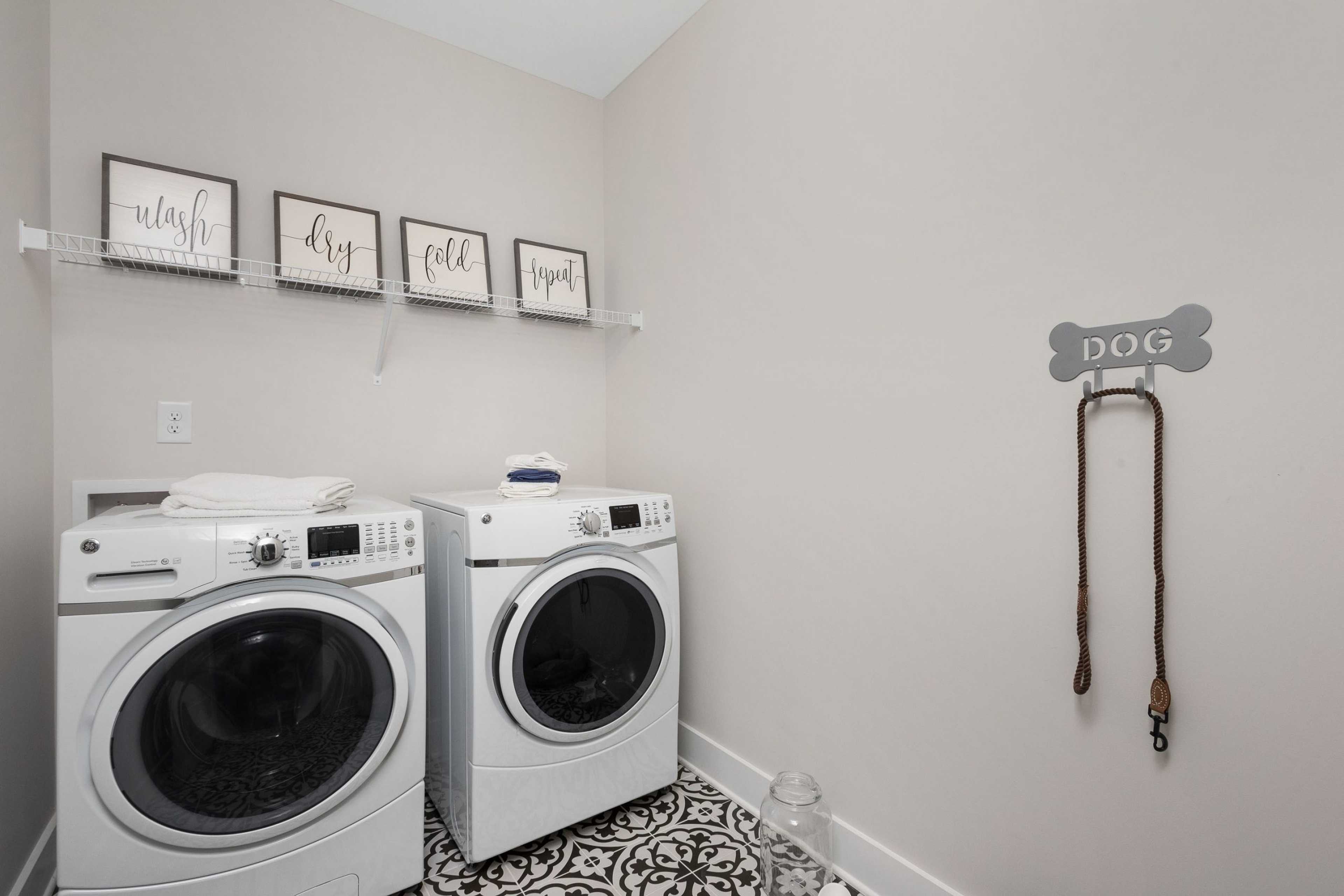 Pet-friendly laundry room at Rivers Edge in Murfreesboro TN with white washer dryer set, wash dry fold signs, and dog leash hook