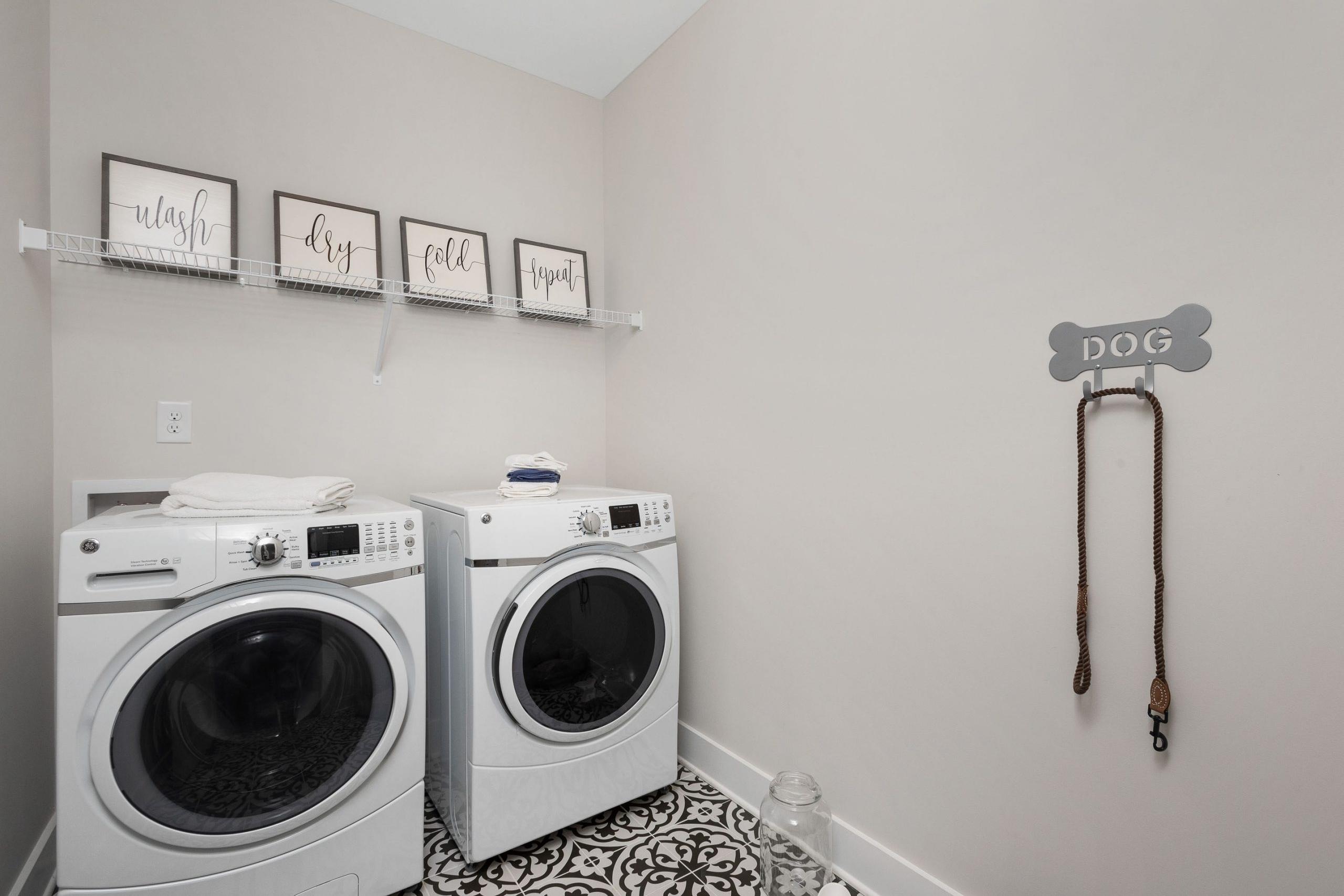 Pet-friendly laundry room at Rivers Edge in Murfreesboro TN with white washer dryer set, wash dry fold signs, and dog leash hook