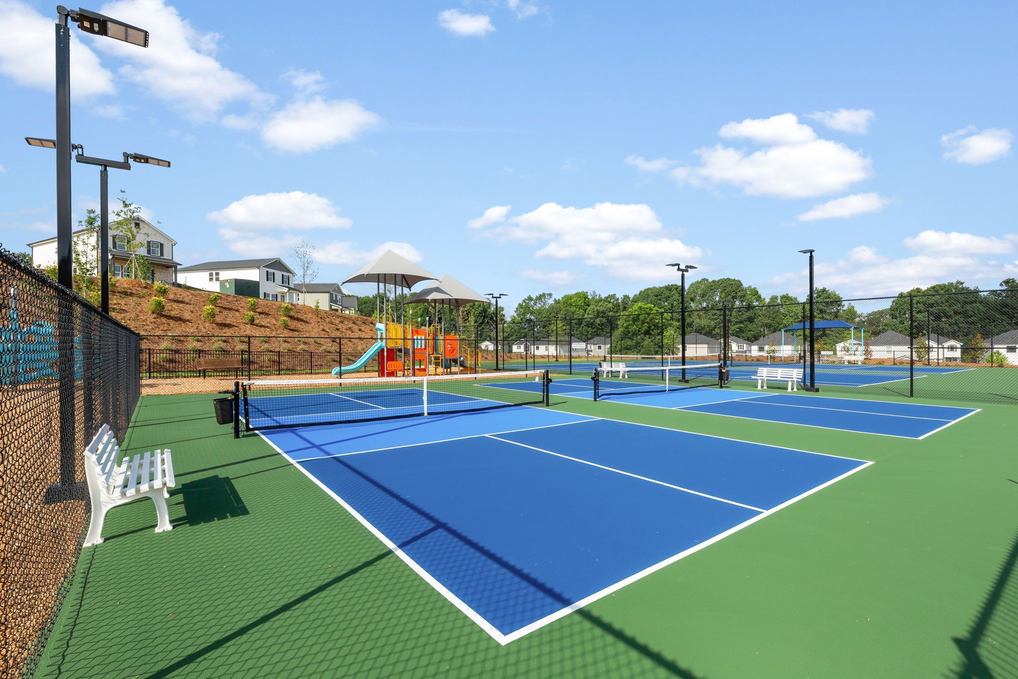 Tennis courts and playground at Hemingway in Cumming GA with blue courts benches fencing and modern homes backdrop