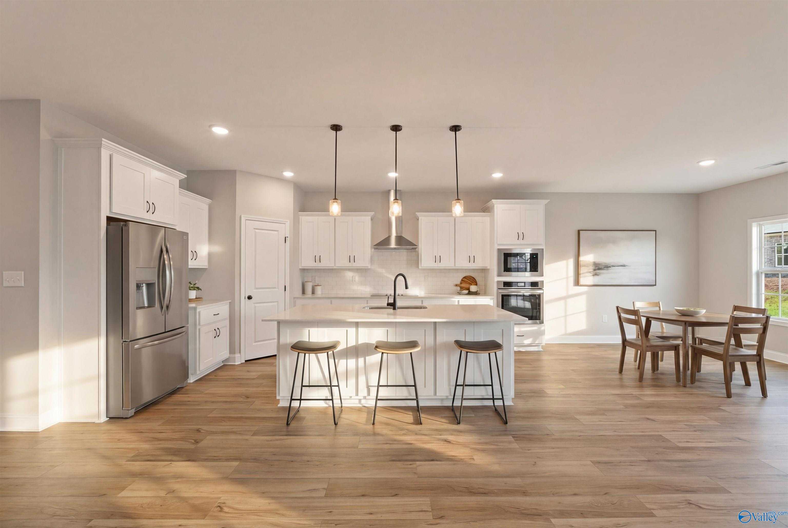 Modern white kitchen featuring large island, stainless fridge, pendant lights, and open dining area in Davidson Homes The Rockford, Toney, Alabama