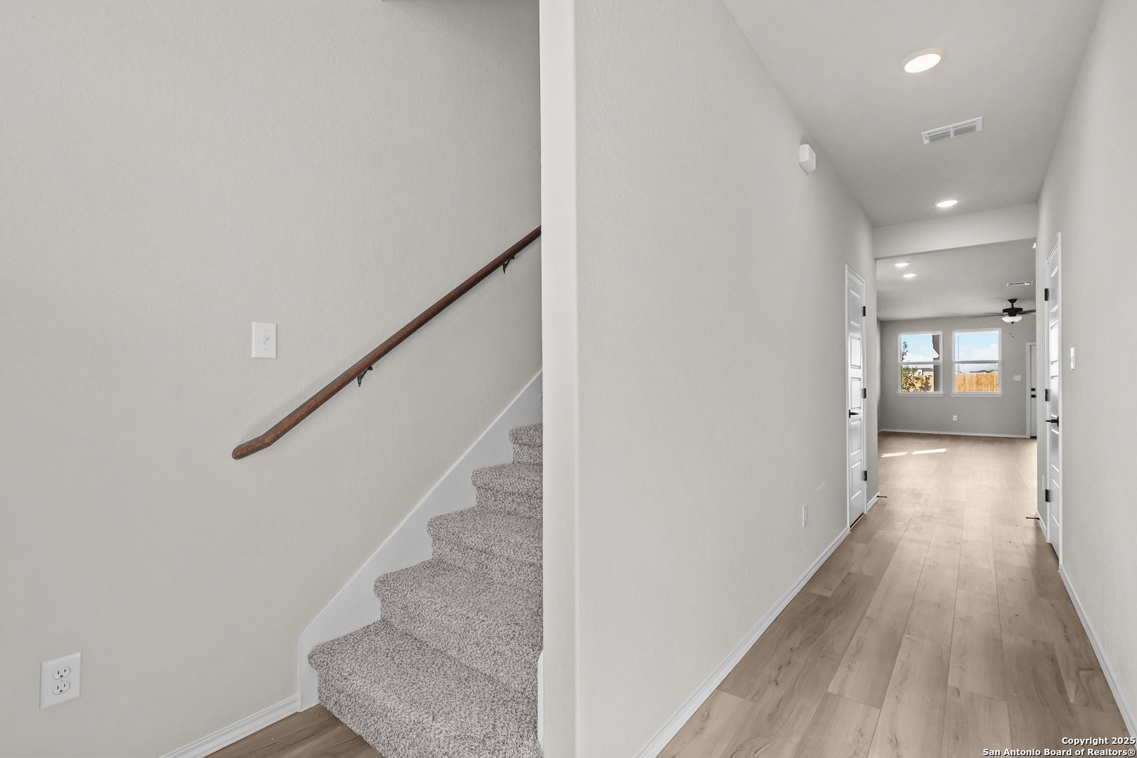 Elegant carpeted staircase with wooden handrail and adjacent hardwood hallway in The Brazos C 5-bedroom home, Applewhite Meadows, San Antonio
