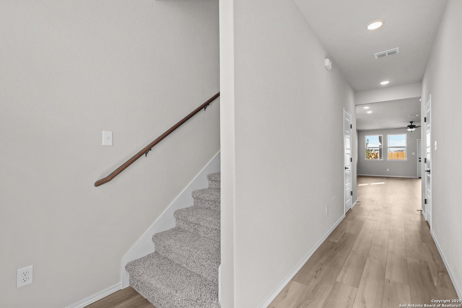 Elegant carpeted staircase with wooden handrail and adjacent hardwood hallway in The Brazos C 5-bedroom home, Applewhite Meadows, San Antonio
