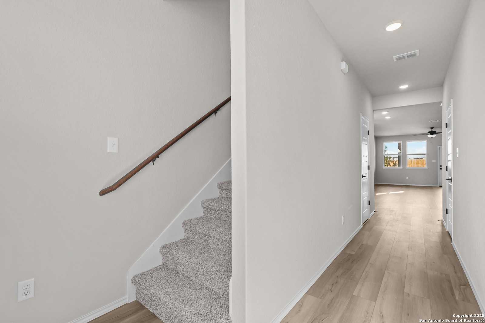 Elegant carpeted staircase with wooden handrail and adjacent hardwood hallway in The Brazos C 5-bedroom home, Applewhite Meadows, San Antonio