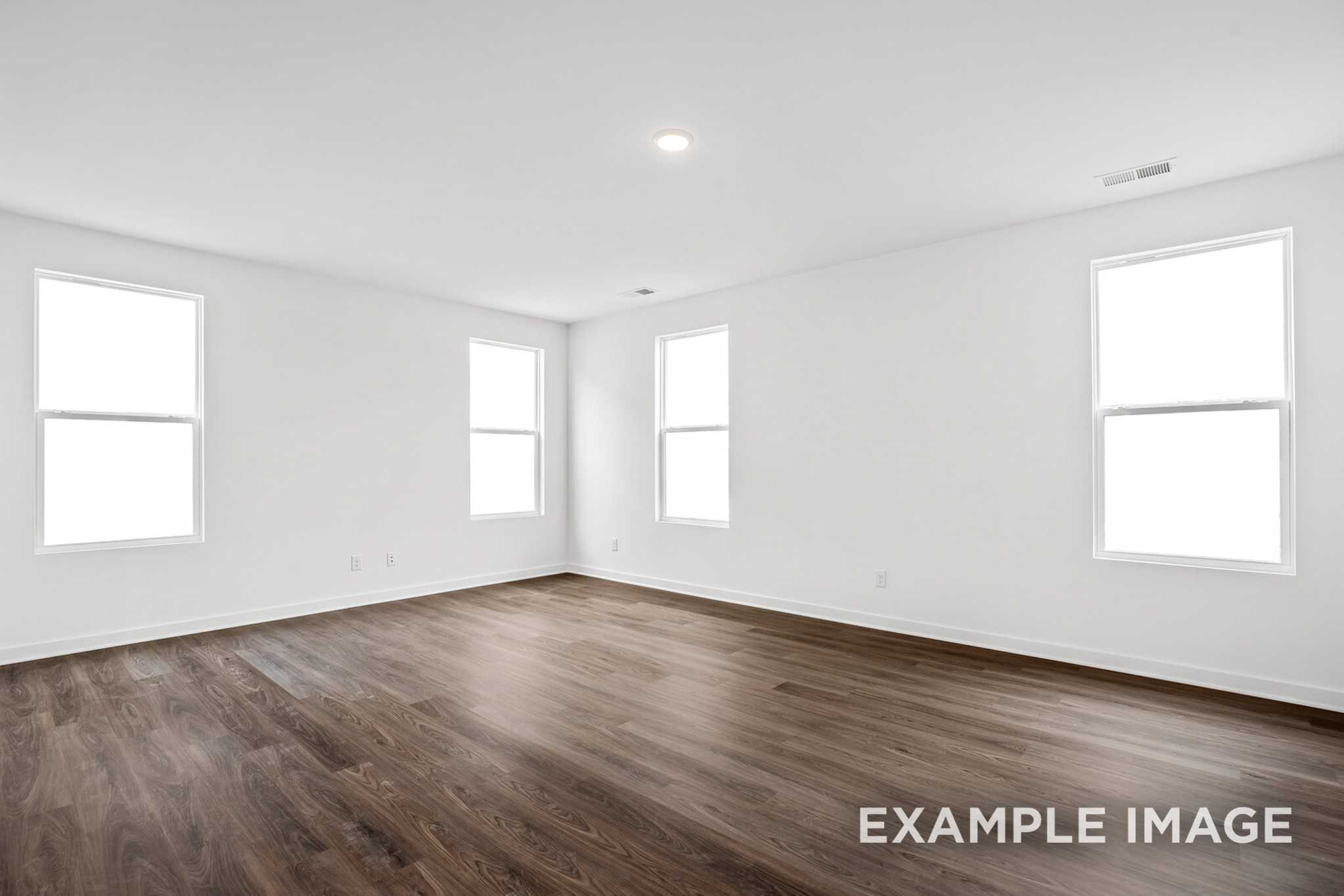Spacious empty room in The Grayson C home with white walls, large windows, and dark hardwood floors