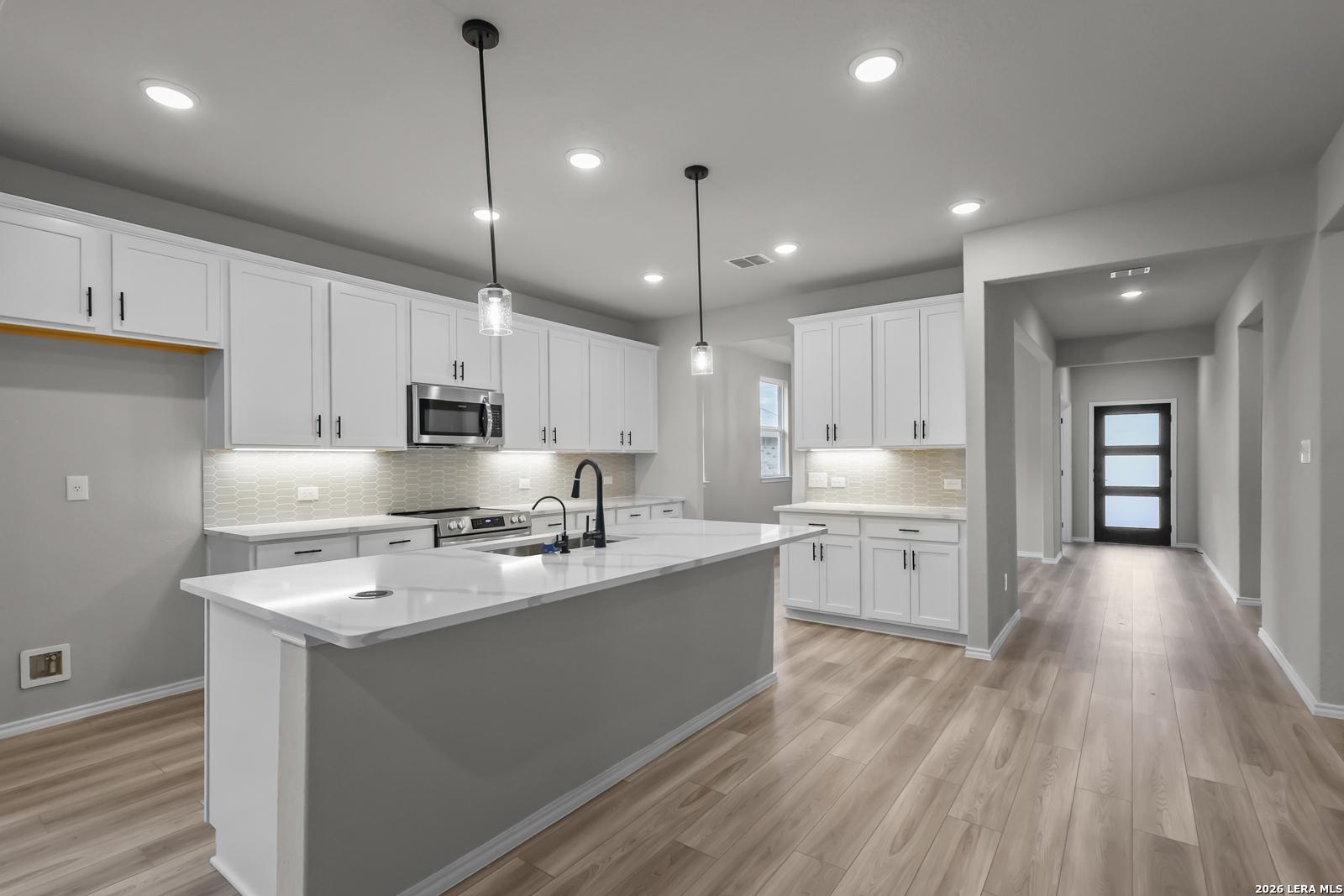 Modern open-concept kitchen featuring white shaker cabinets, quartz island, stainless appliances in The Glenwood F, Davidson Homes, San Antonio