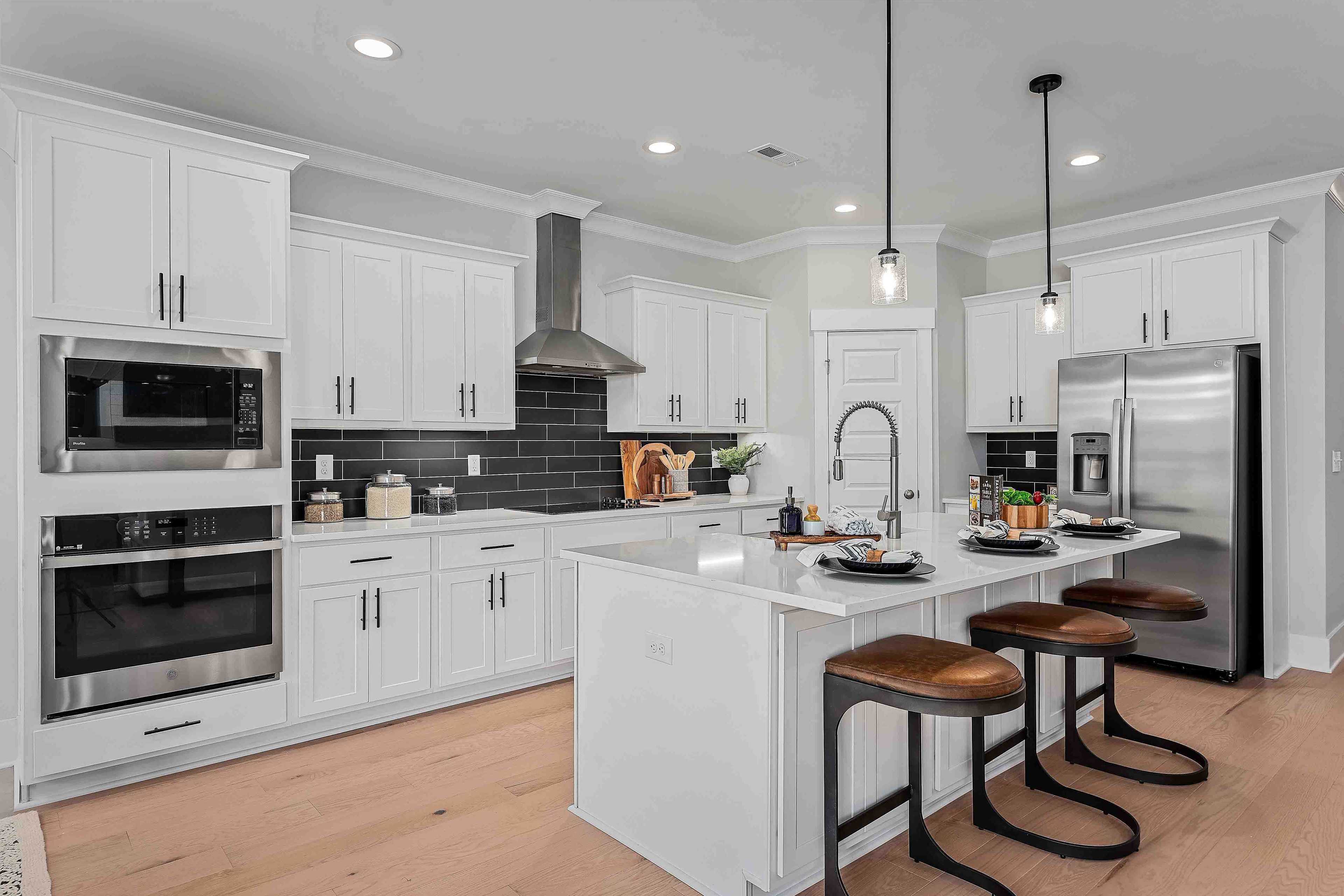 Modern white kitchen at Cain Park in Hartselle AL with island bar stools, stainless appliances and hardwood floors