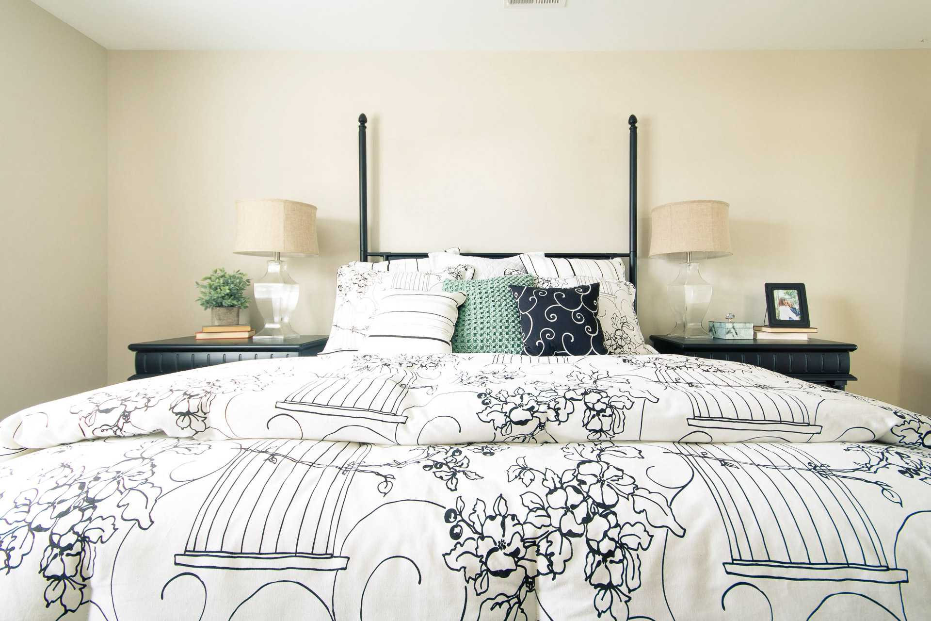 Cozy master bedroom at Summer Pointe in Madison Alabama with poster bed, floral duvet, pillows, and bedside lamps