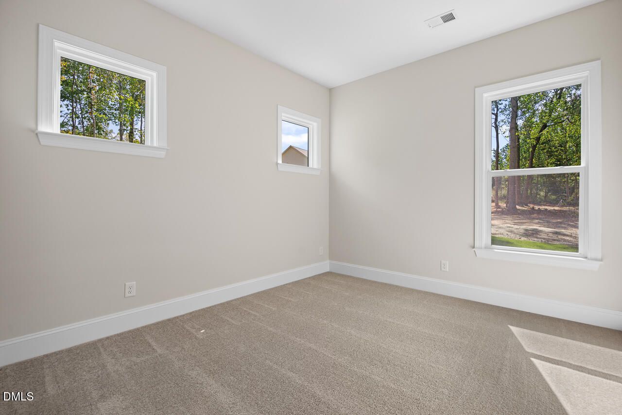 Bright carpeted bedroom with multiple windows overlooking wooded views in Davidson Homes The Crawford D, Rockport, Wake Forest, NC