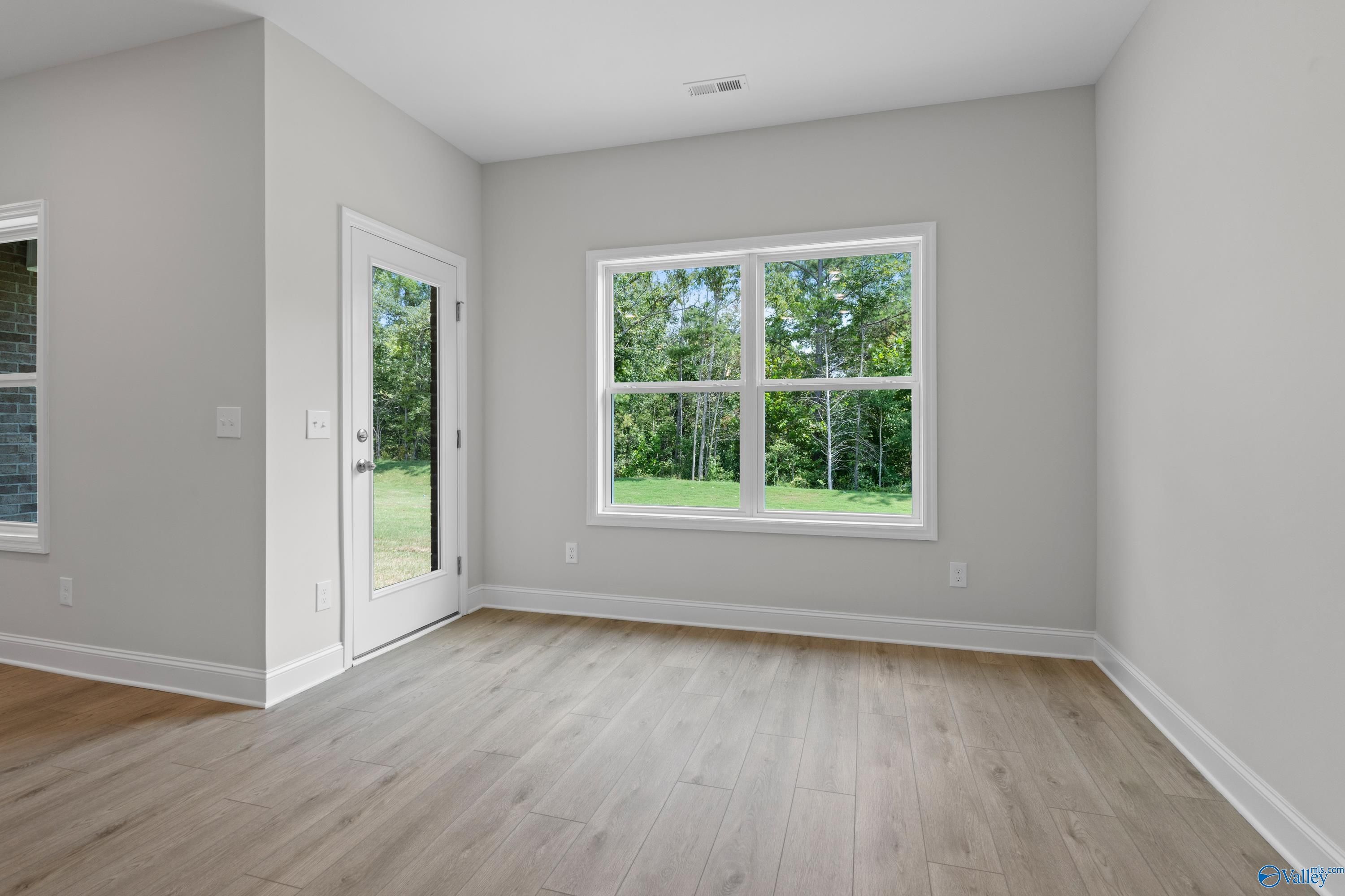 Bright sunlit room with large windows, glass door to wooded yard, hardwood floors in The Asheville 3-bedroom home, Huntsville AL