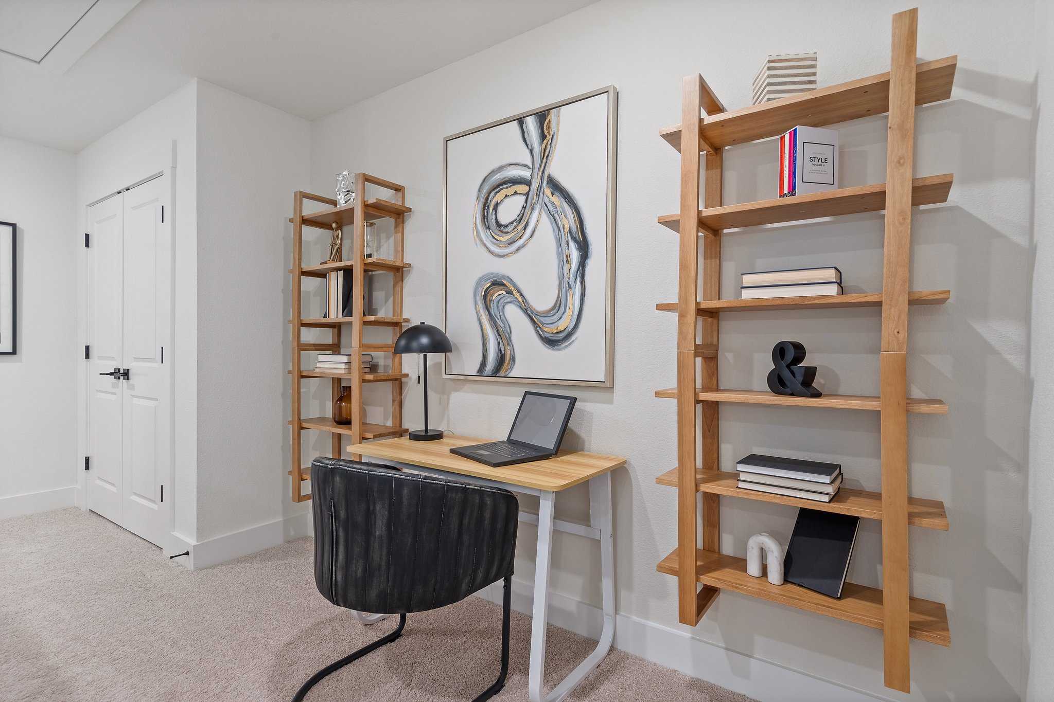 Modern home office in Lake Park Villas Wylie TX with oak bookshelves, abstract art, wooden desk, laptop, and black chair