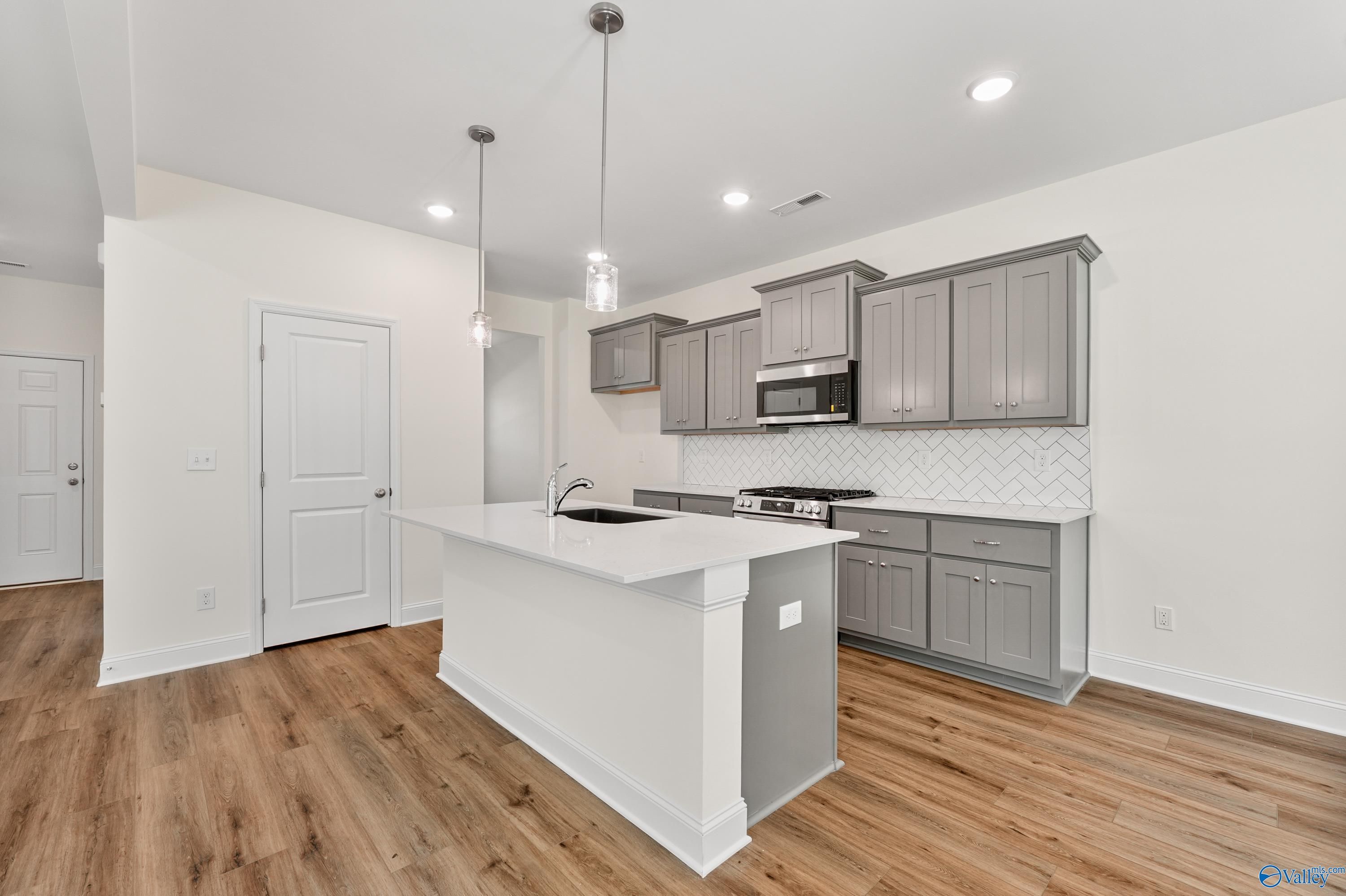 Modern kitchen with white quartz island sink, gray shaker cabinets, stainless microwave, subway tile backsplash in Davidson Homes Shelby A, Athens AL