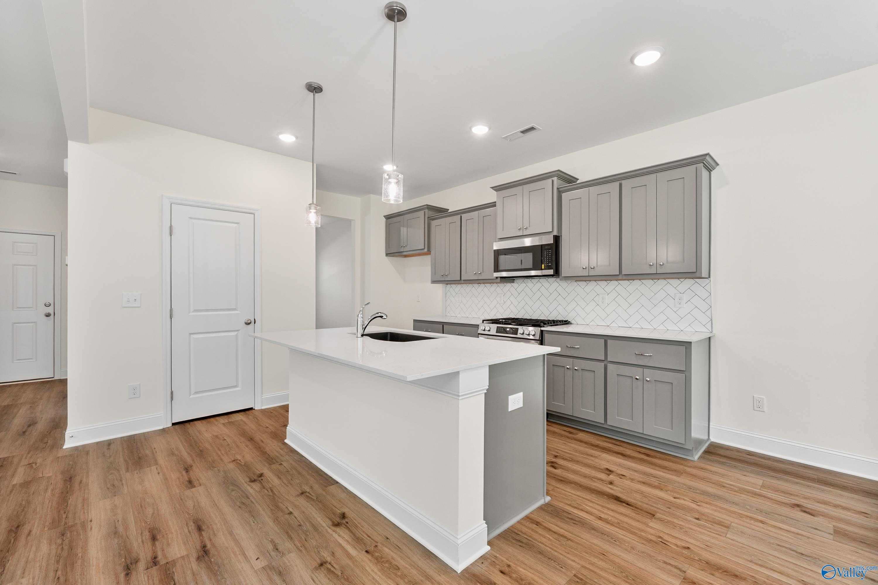Modern kitchen with white island sink, gray shaker cabinets, subway tile backsplash, hardwood floors in The Shelby A by Davidson Homes, Athens AL