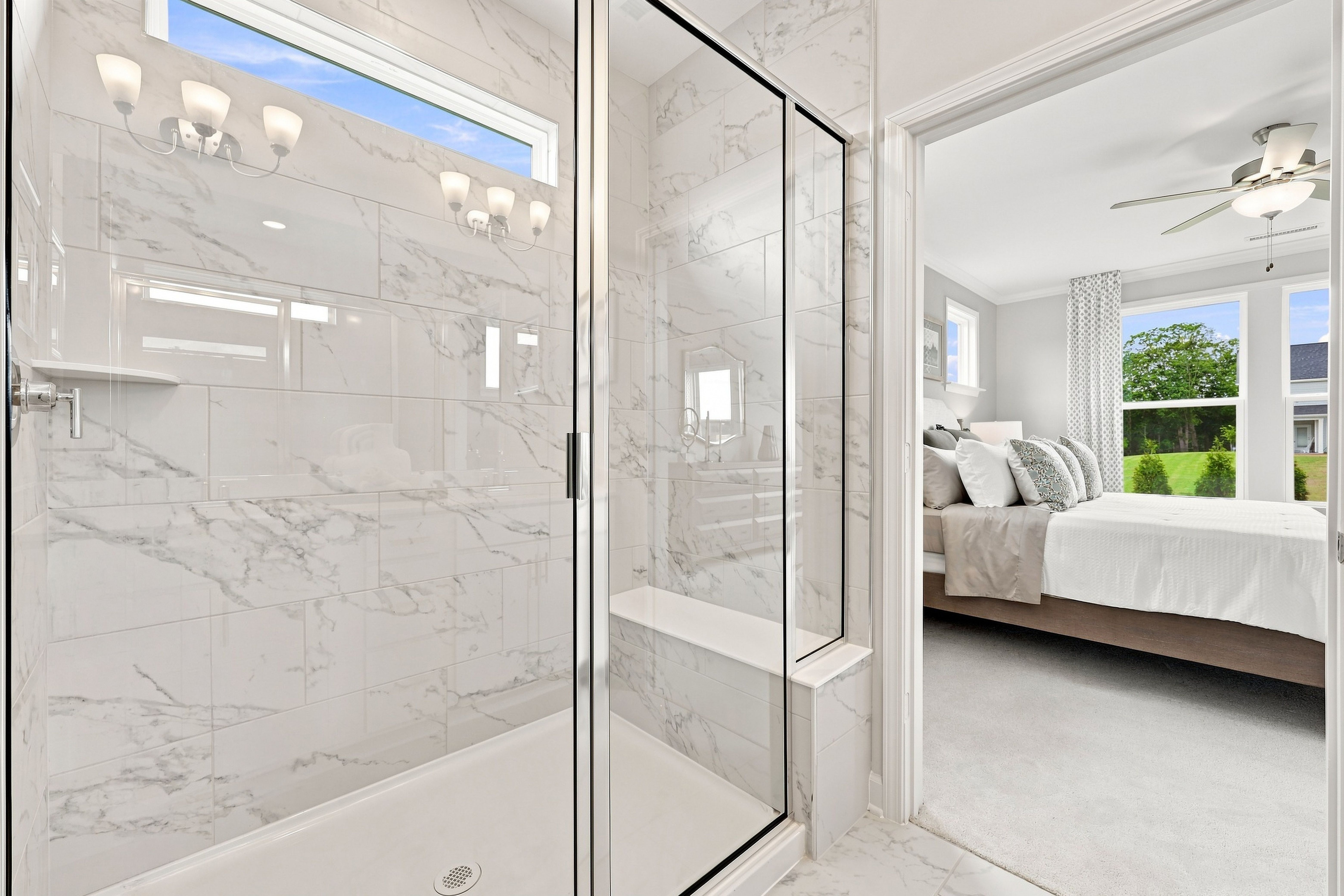 Luxurious master bathroom shower with marble tile and bench seat in The Daphne D home design featuring a main floor suite.