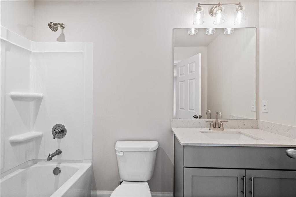 Clean modern bathroom with white tub-shower combo, gray vanity, mirror in Davidson Homes The Hickory B at Wehunt Meadows, Hoschton