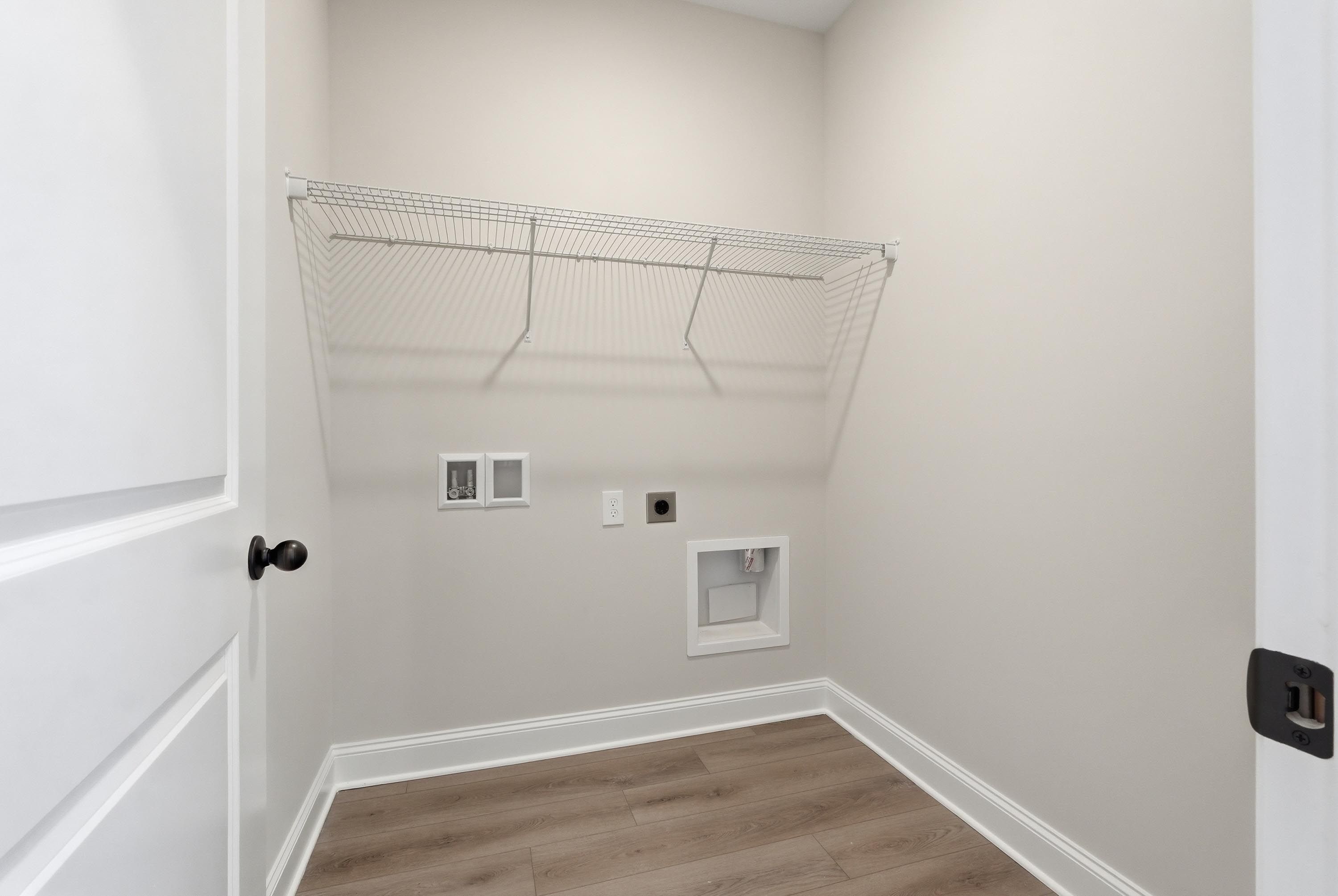 Dedicated laundry room in The Glen A featuring washer and dryer hookups with overhead shelving and wood-plank flooring.