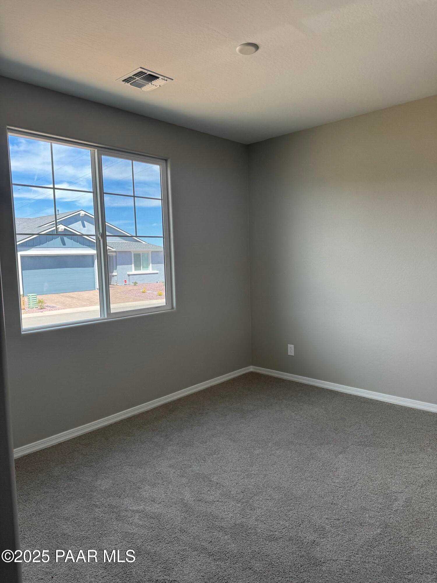 Spacious empty bedroom with beige walls, large grid window overlooking neighborhood, and gray carpet in Davidson Homes The Sheridan II B, Prescott AZ