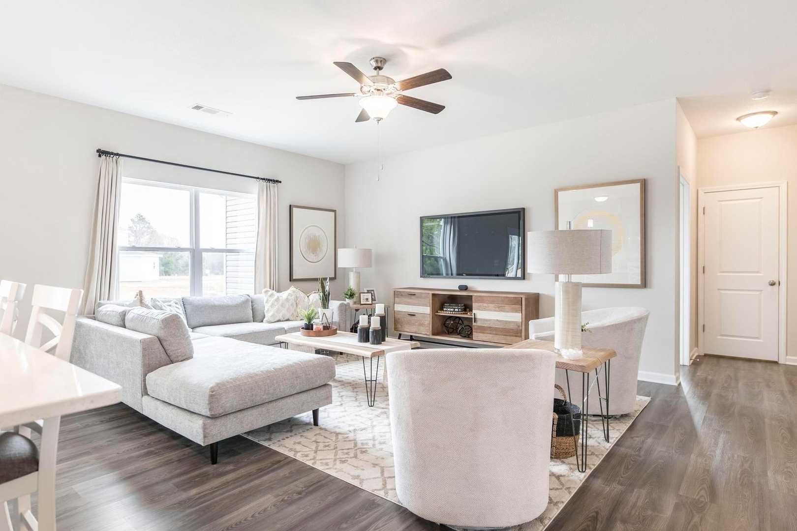 Open-concept living room at Cape Reserve at Donahue Ridge in Auburn Alabama with gray L-shaped sofa, hardwood floors, ceiling fan, and TV media console