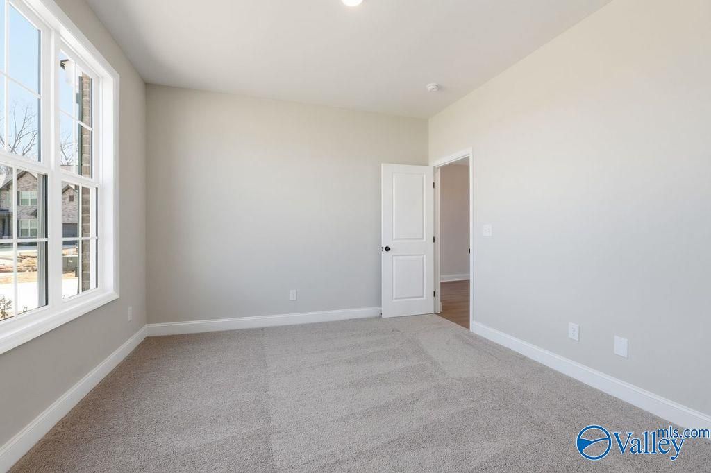 Bright empty bedroom with large windows, neutral beige walls, and gray carpet in Davidson Homes The Montgomery B, Hartselle, AL
