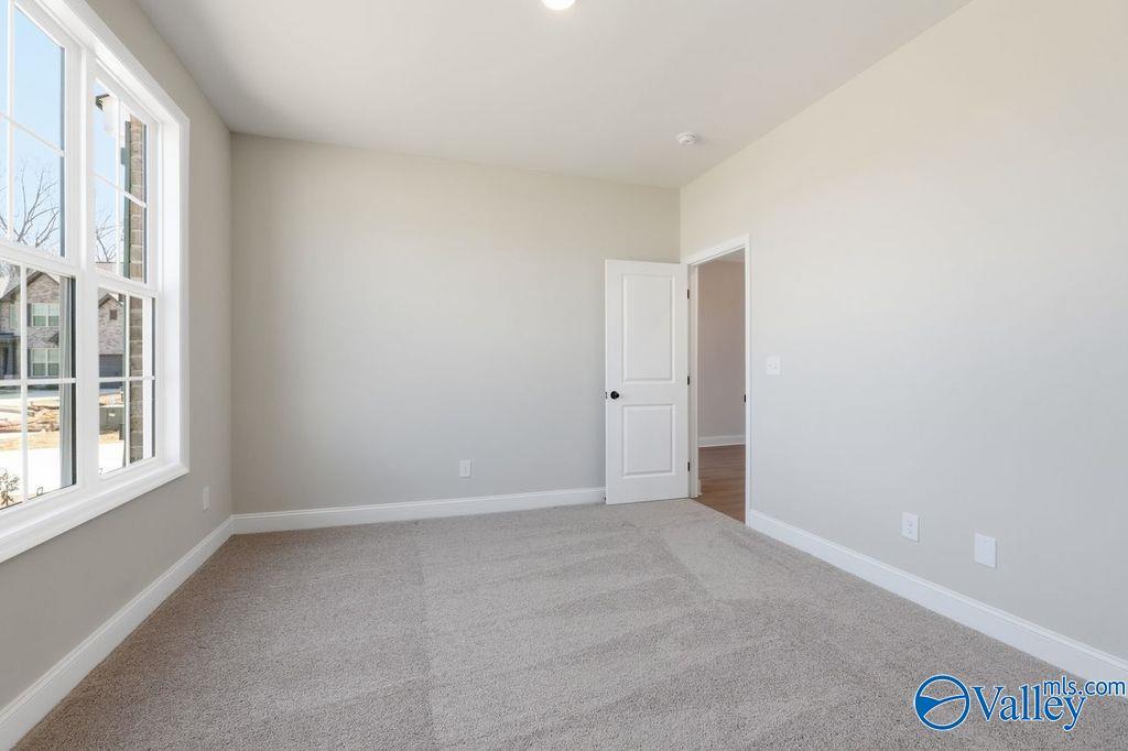 Bright empty bedroom with large windows, neutral beige walls, and gray carpet in Davidson Homes The Montgomery B, Hartselle, AL