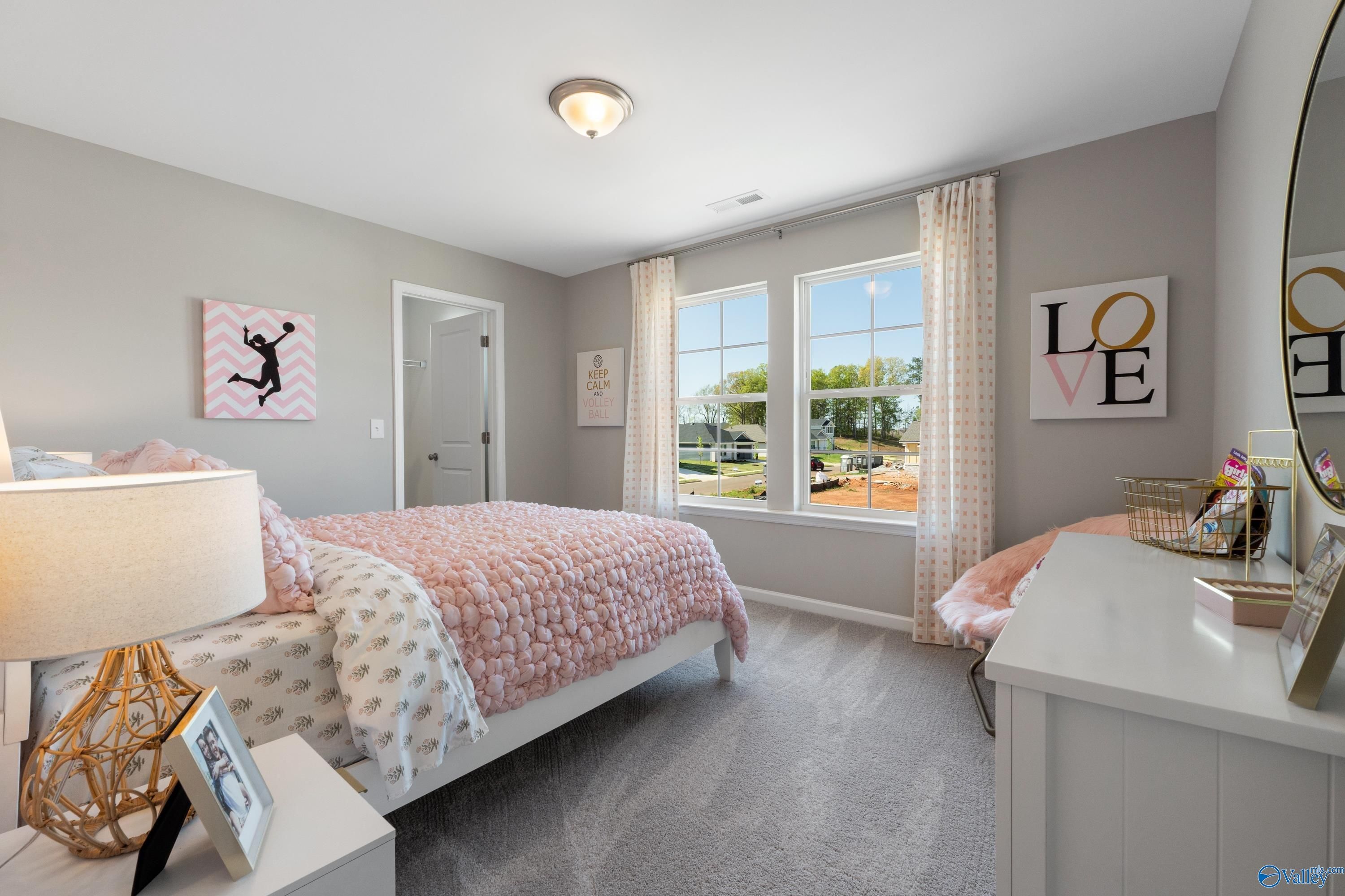 Charming girl's bedroom featuring pink quilted bed, volleyball wall art, vanity mirror, and neighborhood view windows in Davidson Homes The Stella, Madison, Alabama