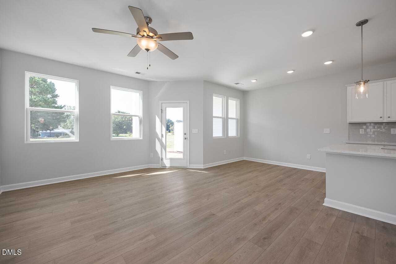 Bright open living room with ceiling fan, large windows, hardwood floors, and kitchen peninsula in Davidson Homes The Graham, Fuquay-Varina, NC
