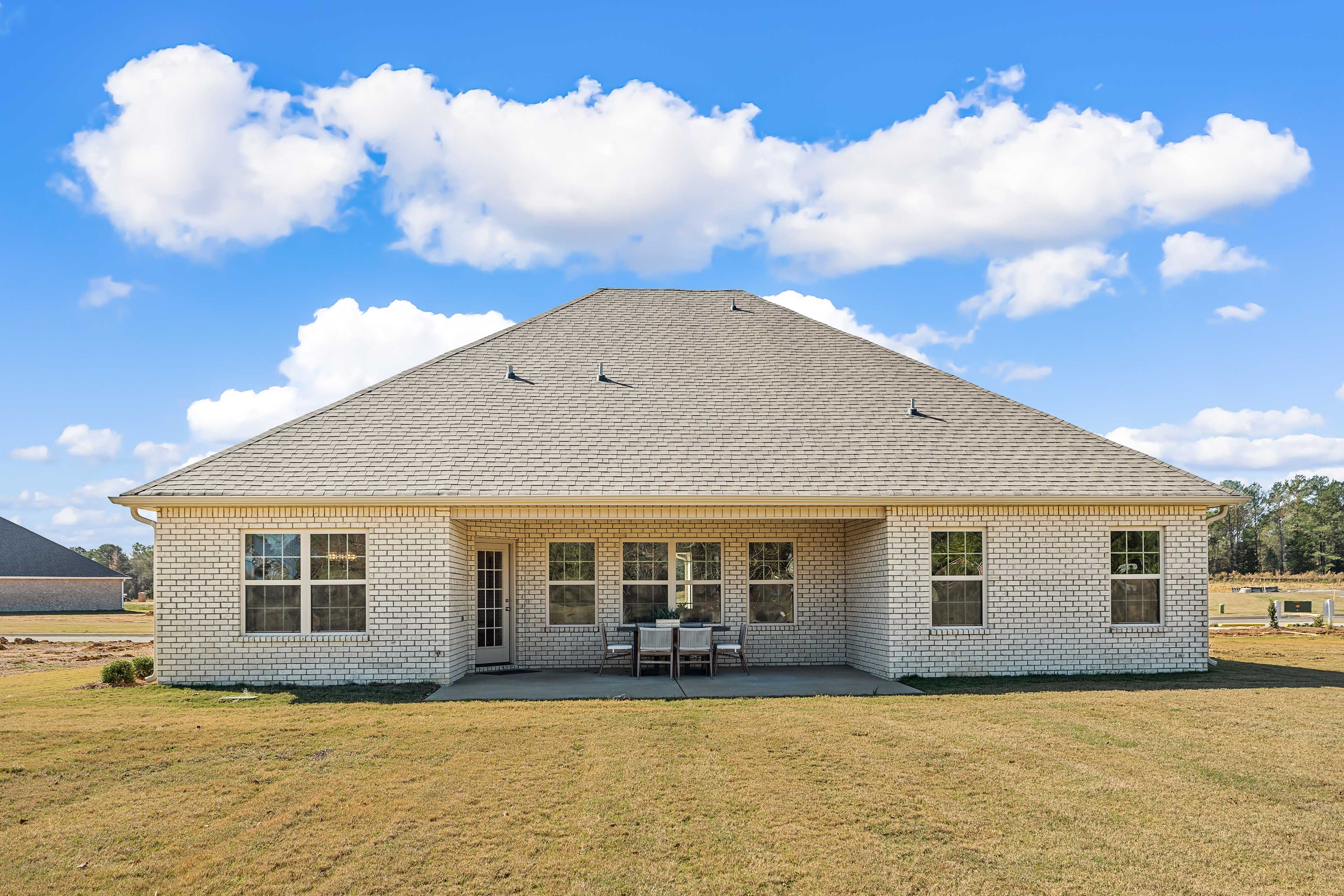 Back exterior of beige brick home at Cain Park in Hartselle Alabama with covered patio and outdoor seating