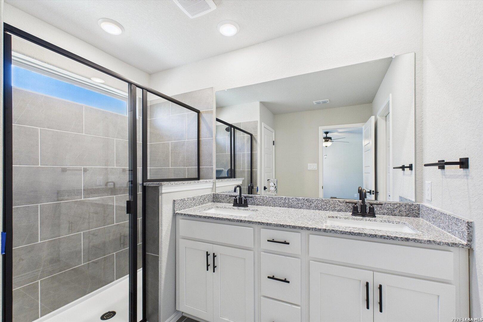 Modern master bathroom with glass-enclosed shower, granite double vanity, and gray tile accents in Davidson Homes Charlotte A, San Antonio