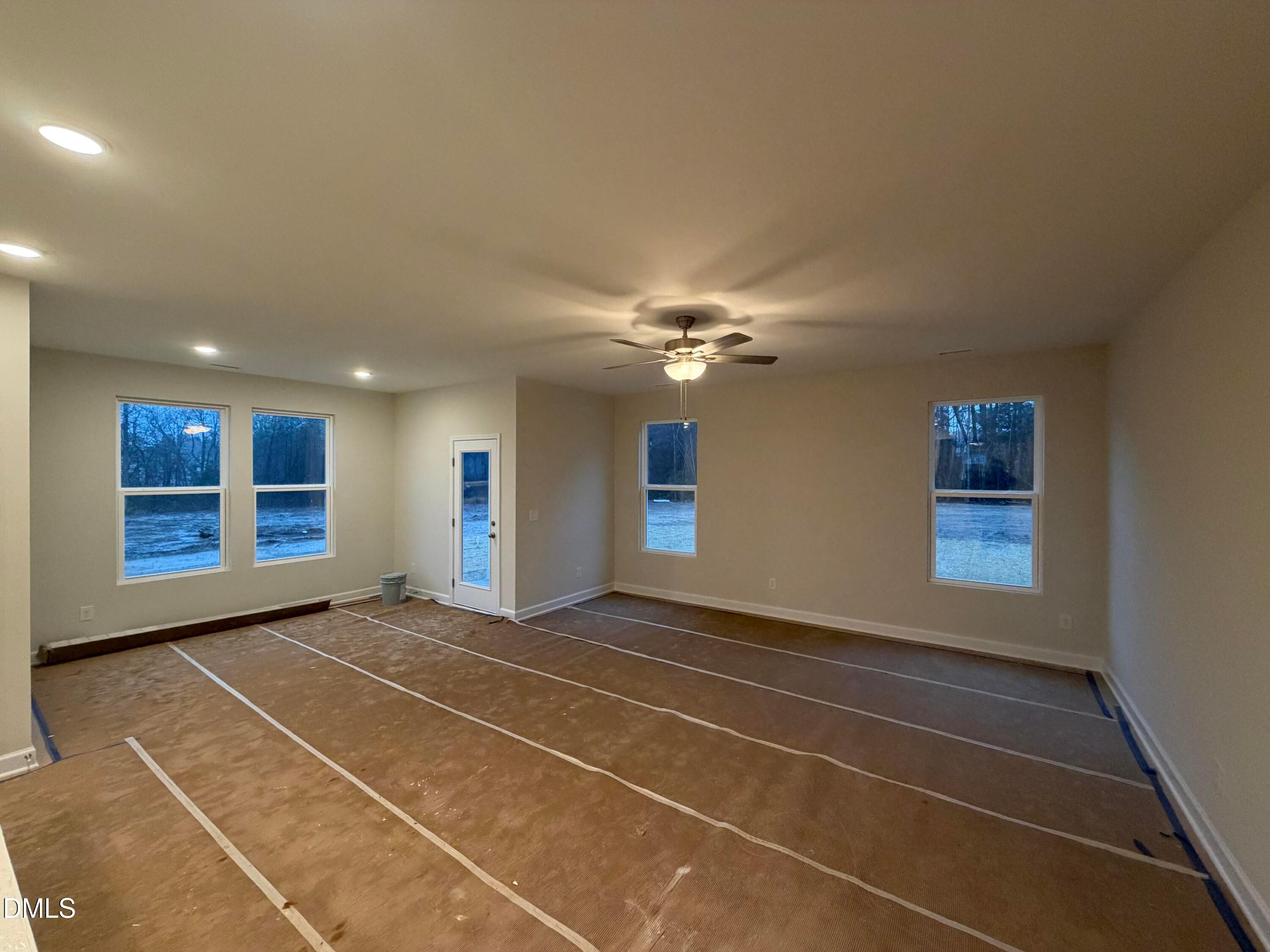 Bright spacious living room with large windows, ceiling fan, and protective flooring in The Daphne C floor plan, Lillington, NC