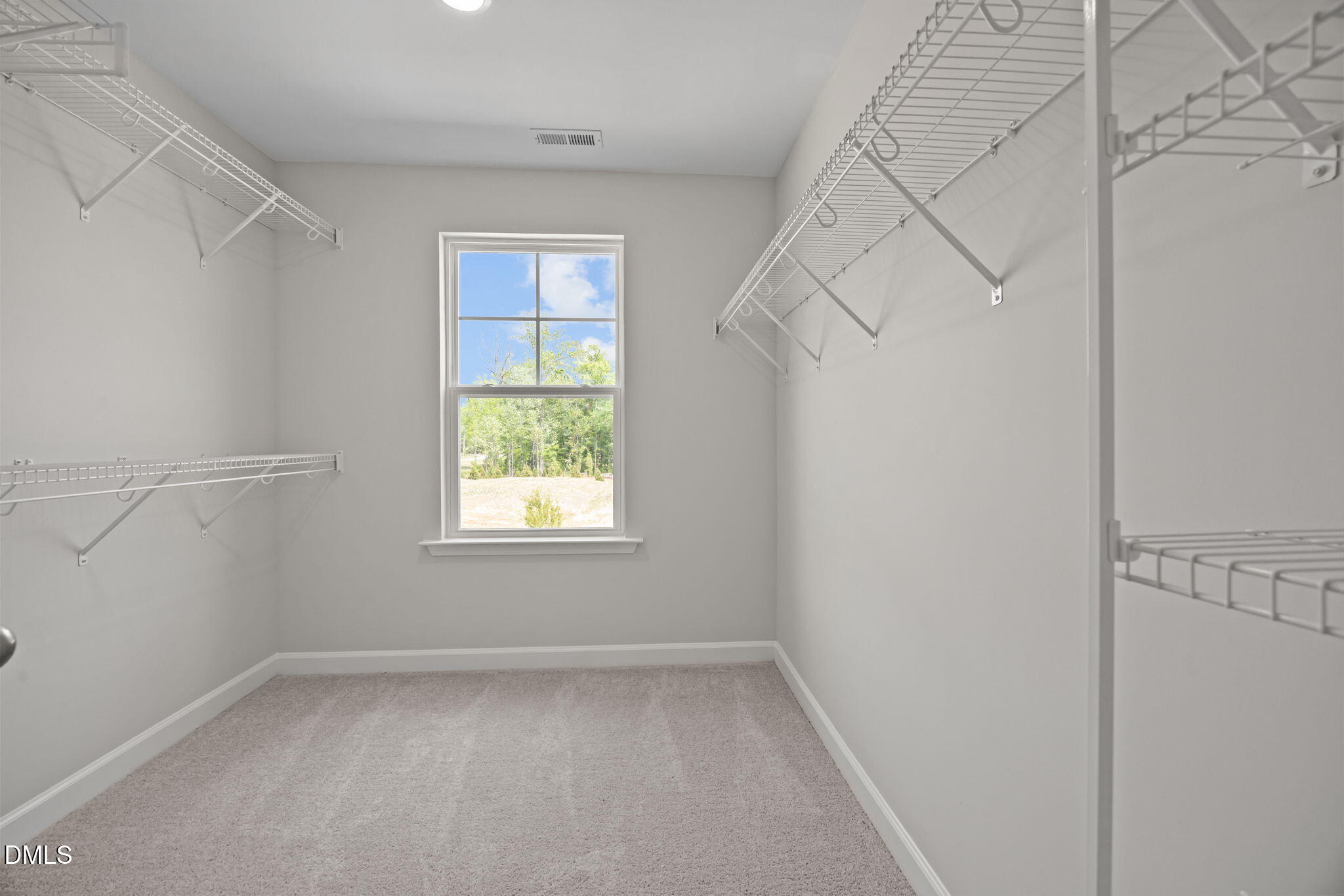 Spacious walk-in closet with white wire shelving, beige carpet, and window view in Davidson Homes The Willow D, Wendell, NC