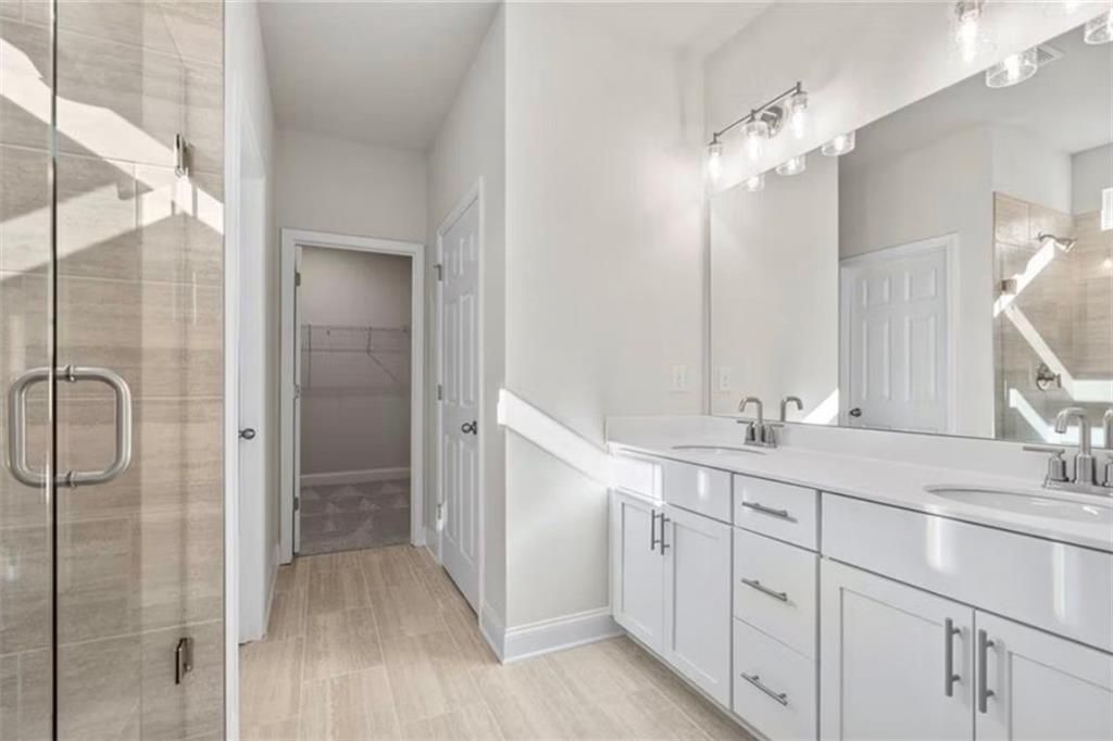 Modern primary bathroom with double vanity and walk-in closet in The Ash C floor plan at Wehunt Meadows, Hoschton, Georgia.
