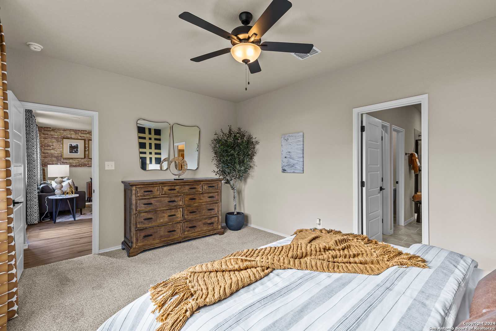 Cozy bedroom with striped duvet bed, wooden dresser, mirrors, and ceiling fan in Davidson Homes The Douglas F, Bricewood, San Antonio