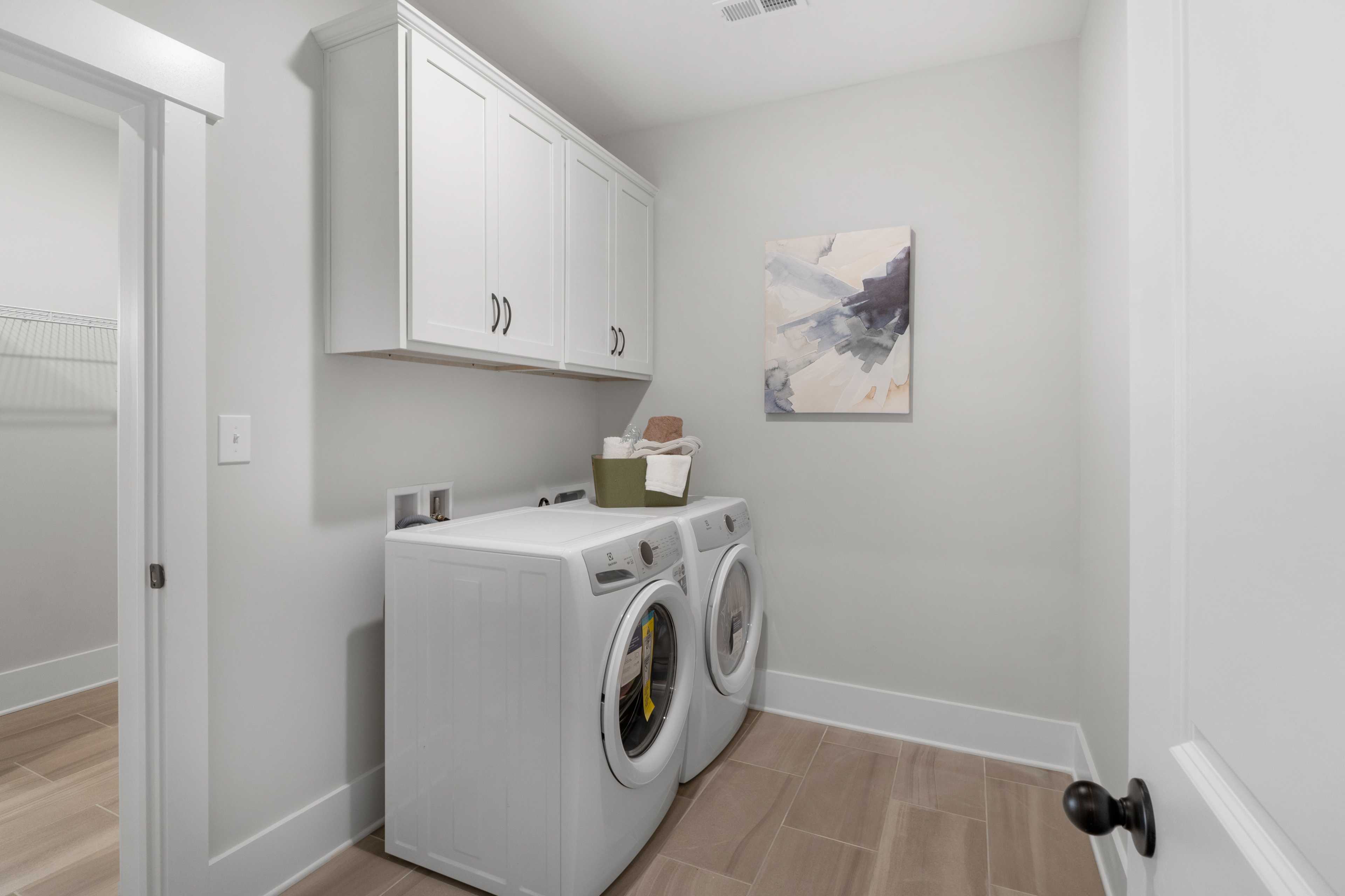 Bright laundry room in Briercreek Meridianville AL home with white washer dryer, cabinets, baskets and light wood floors