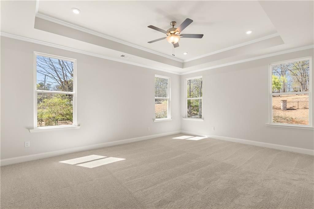 Bright secondary bedroom with beige carpet, light gray walls, large windows overlooking wooded backyard, ceiling fan in The Danbury C, Buford, GA