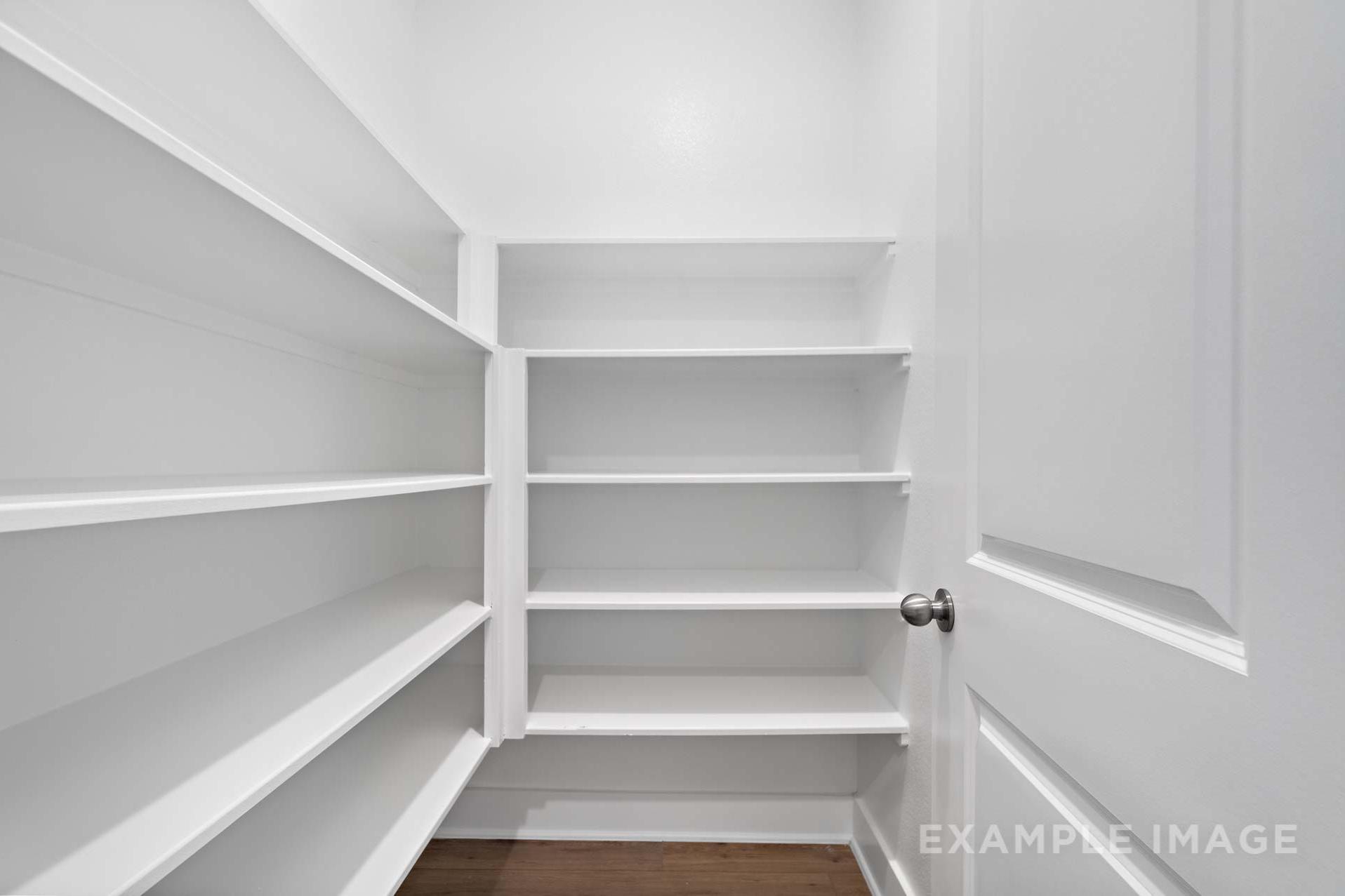 Spacious walk-in closet in The Diana C master suite featuring built-in wooden shelves and open white door