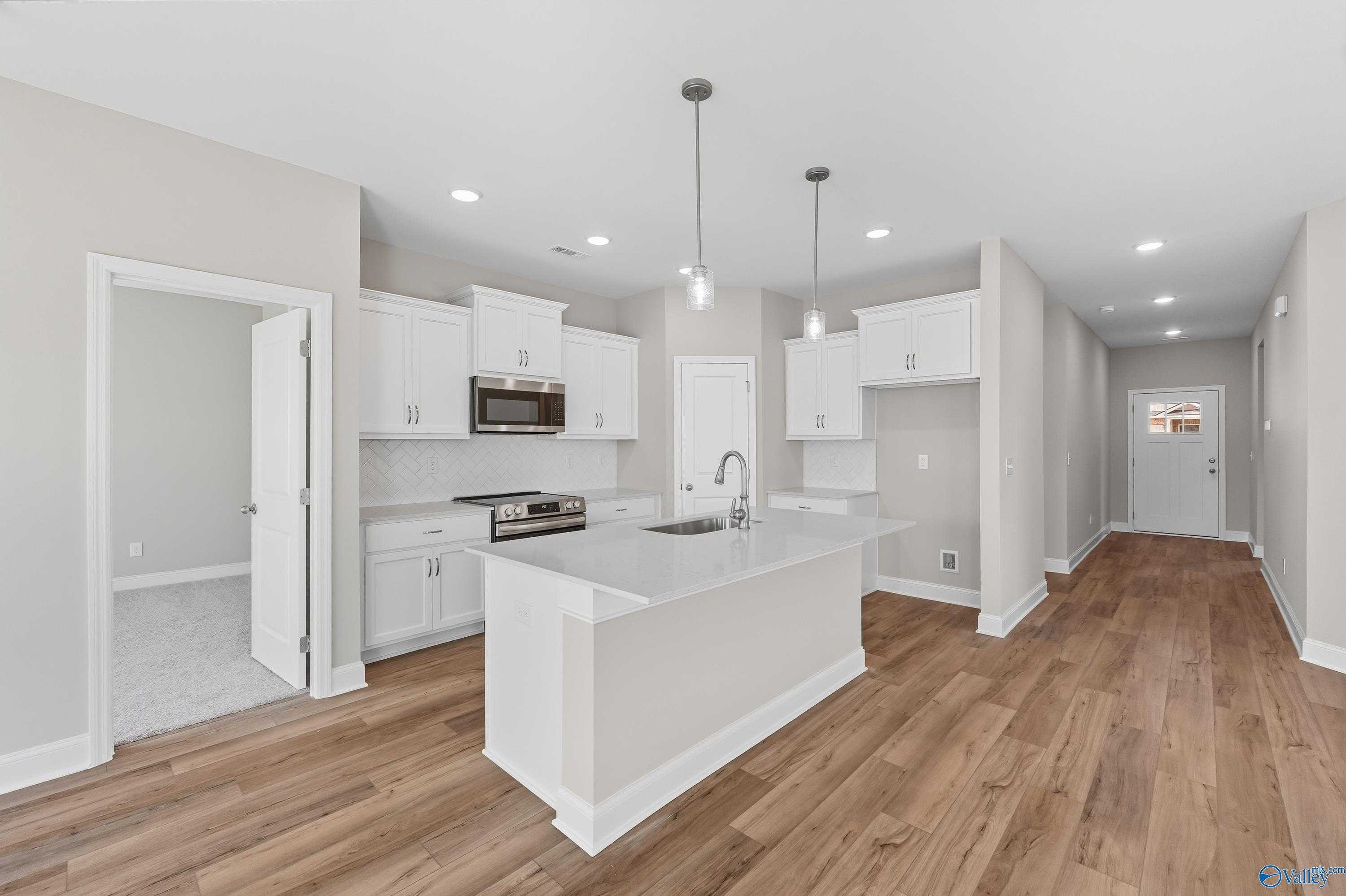 Modern open kitchen featuring white island, stainless appliances, and hardwood floors in The Franklin 3-bedroom home, Meridianville, Alabama