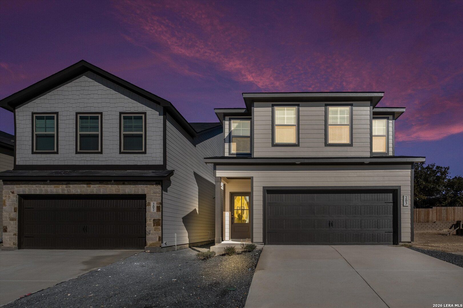 Modern two-story Charlotte A home exterior with two-car garage and stone accents at dusk in Meadows at Oak Creek, San Antonio