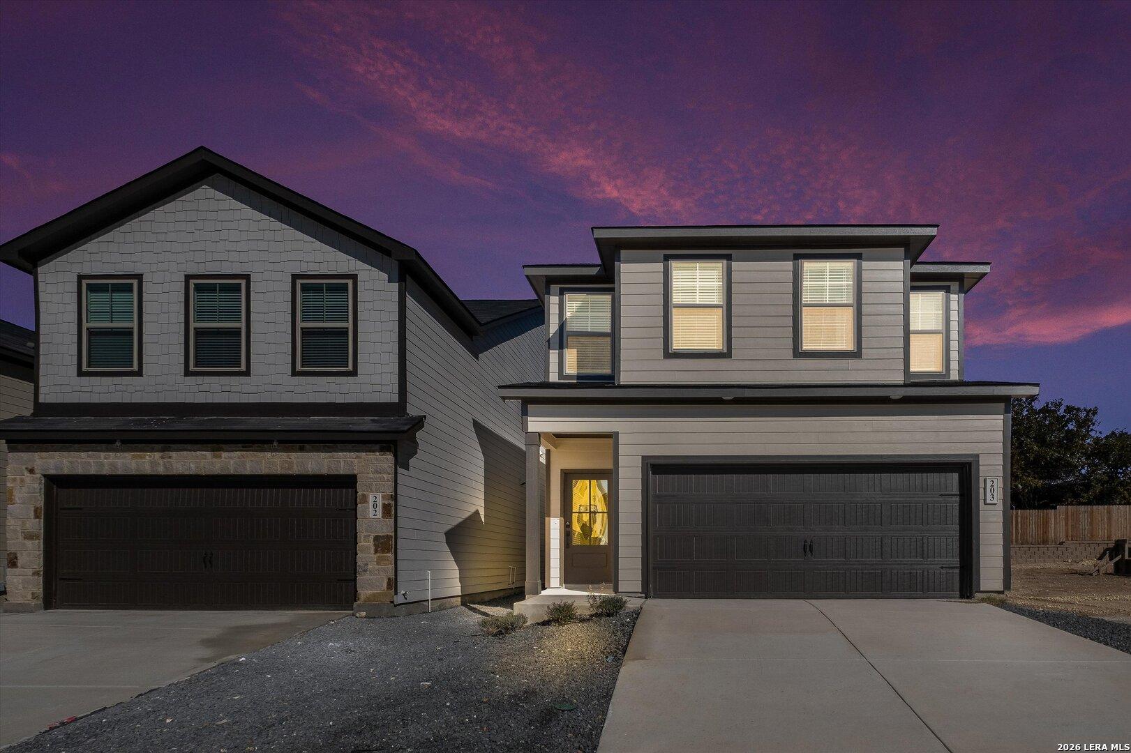 Modern two-story Charlotte A home exterior with two-car garage and stone accents at dusk in Meadows at Oak Creek, San Antonio