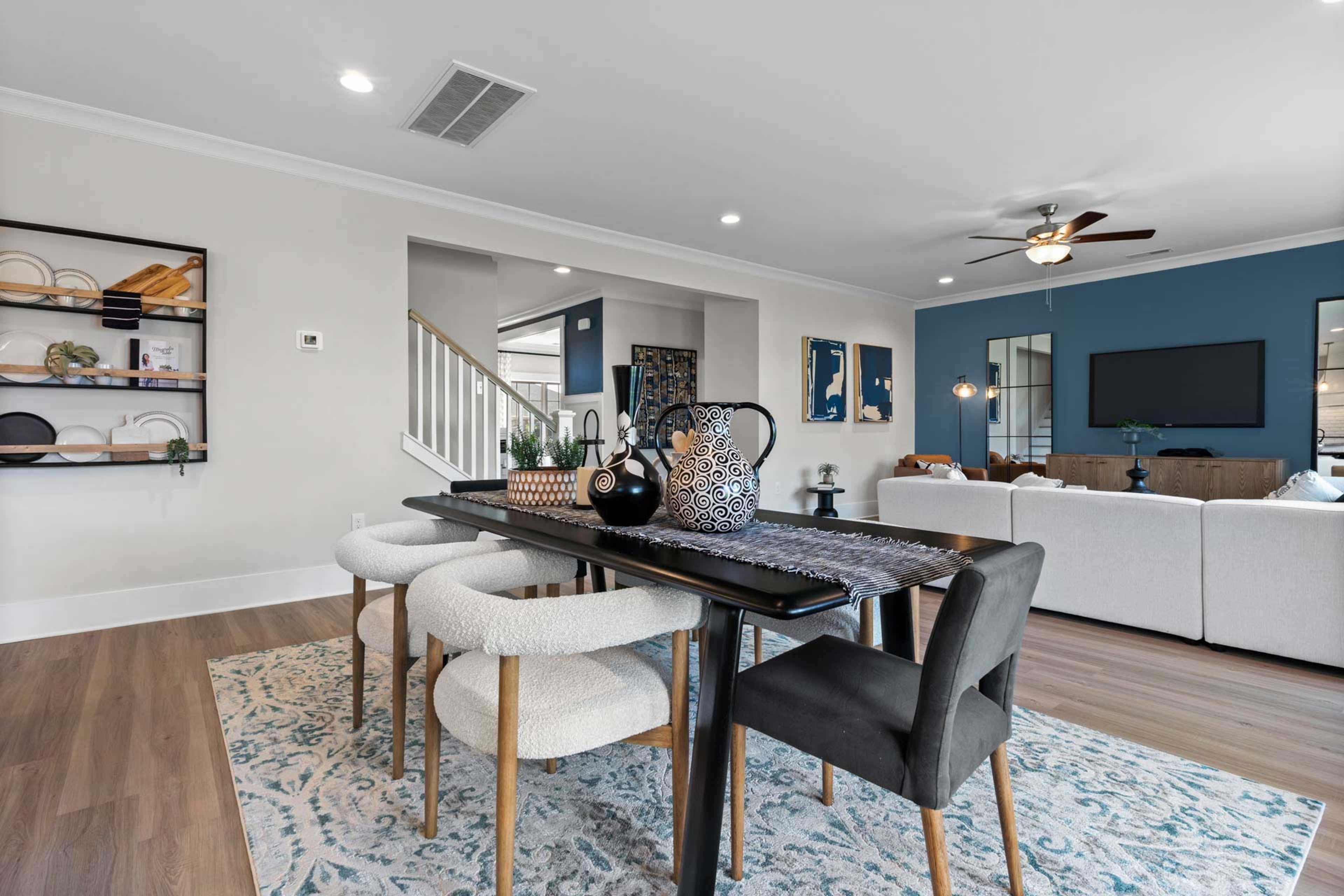 Open-concept dining area at Walker's Hill in Meridianville, Alabama with dark wood table, upholstered chairs, blue accent wall, and white sectional sofa