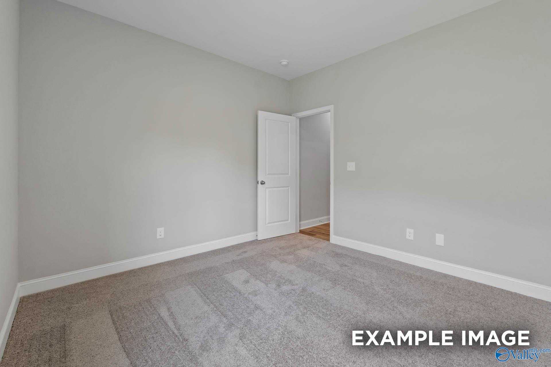 Empty bedroom featuring light gray walls, neutral carpet flooring, and white interior door in Davidson Homes The Everett, Meridianville, Alabama