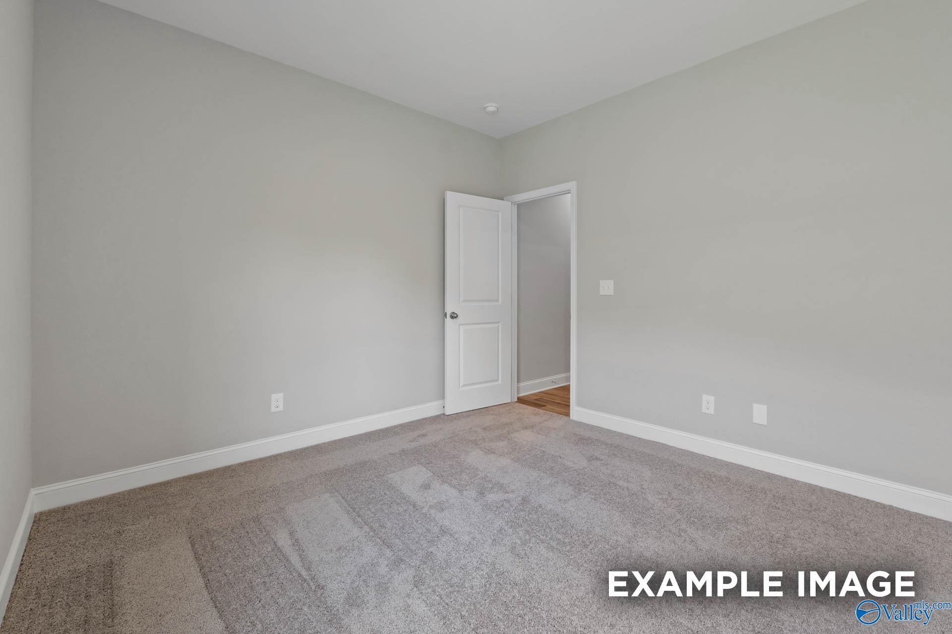 Spacious empty bedroom with neutral gray walls, plush carpet, and open door in Davidson Homes The Everett B, Athens, Alabama