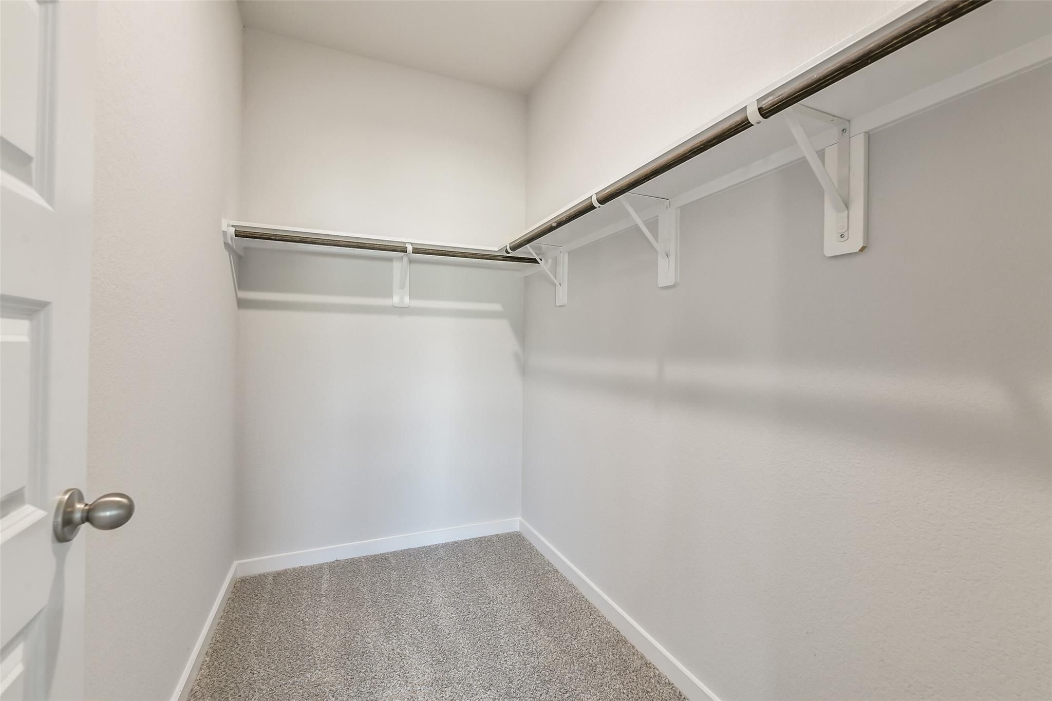 Spacious walk-in closet with white double doors, metal hanging rods, gray carpet in The San Marcos E home, Conroe, Texas