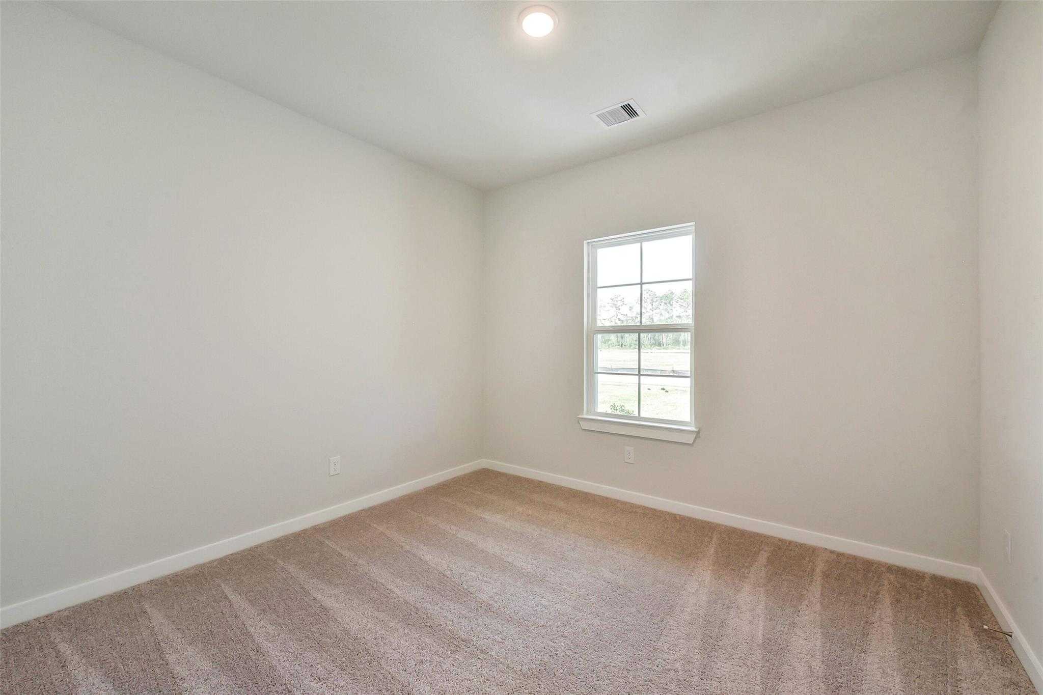 Bright empty bedroom with neutral walls, berber carpet, and large window in Davidson Homes The Comal G, Dayton Texas