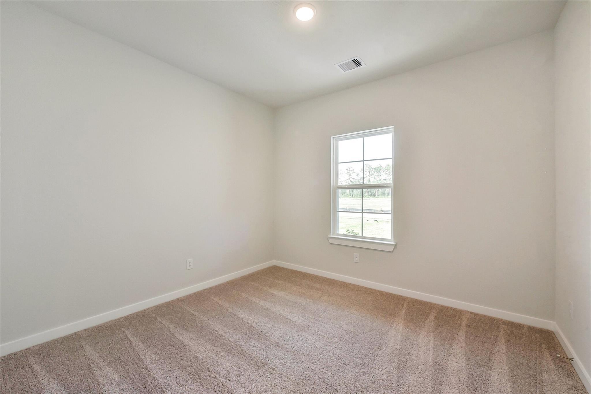 Bright secondary bedroom with neutral walls, large window, plush carpet in Davidson Homes The Comal G, Dayton, Texas