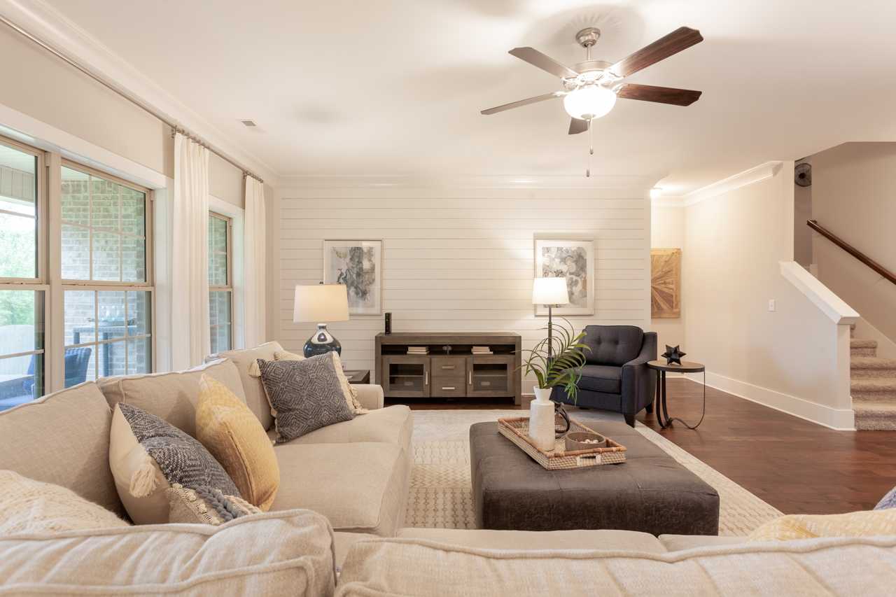 Spacious open-concept living room at Laurenwood Preserve in Madison AL with beige sofa, large windows, hardwood floors, and ceiling fan