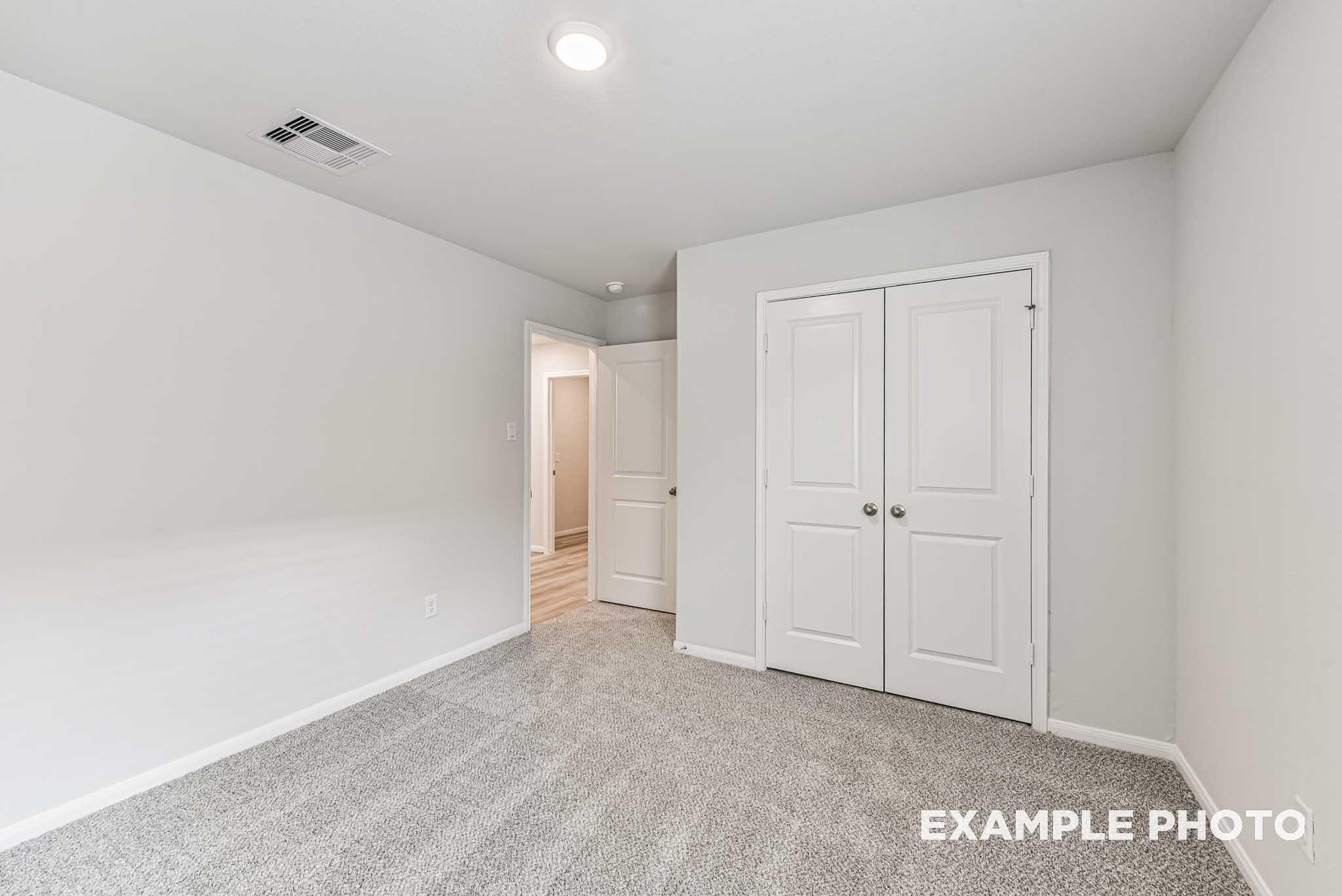 Bright secondary bedroom featuring gray carpet, white walls, and double closet doors in Davidson Homes The Riviera A, Rosharon, Texas
