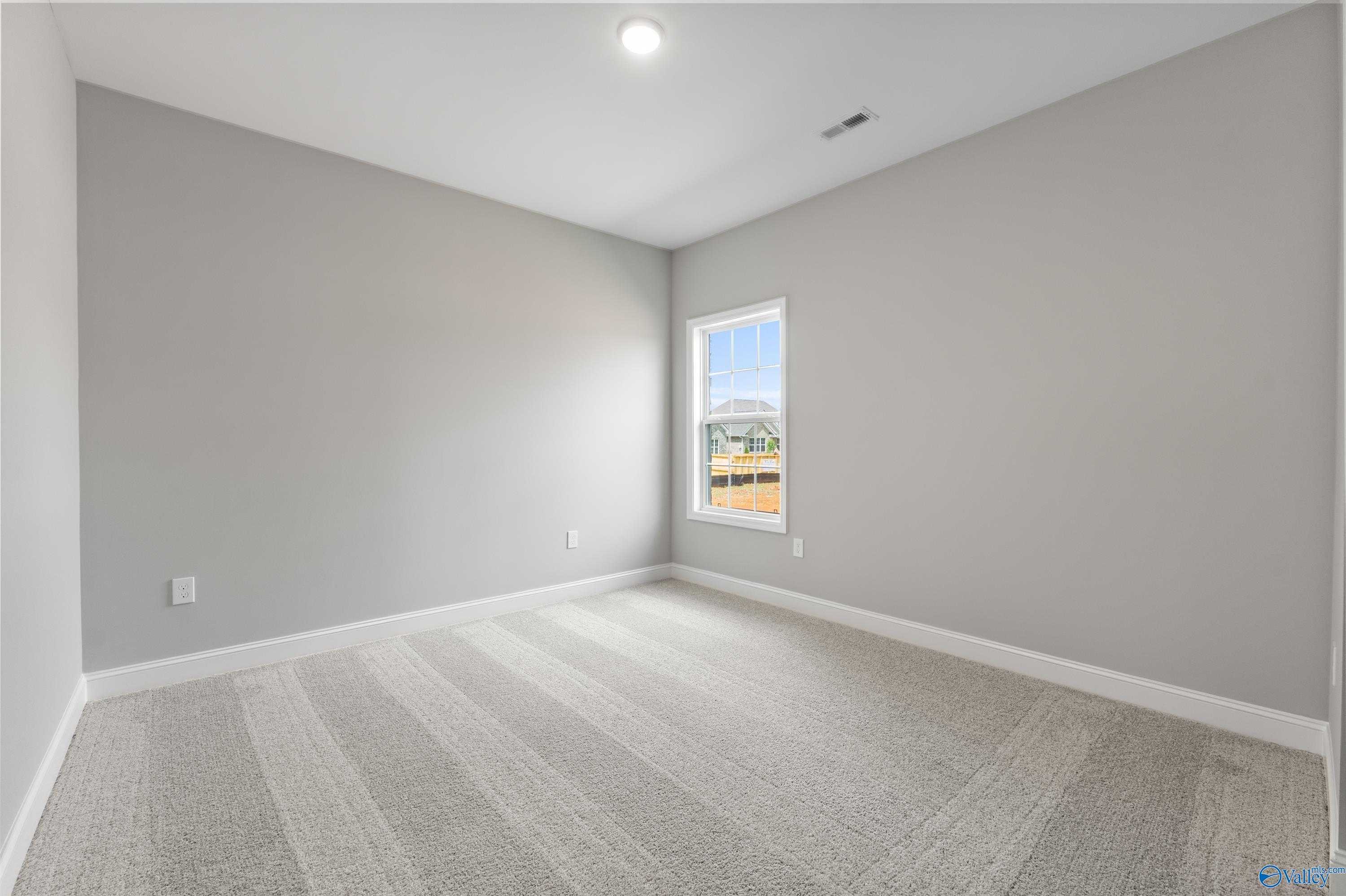 Empty bedroom with light gray walls, large window, and plush carpet in Davidson Homes The Finleigh, Toney, Alabama