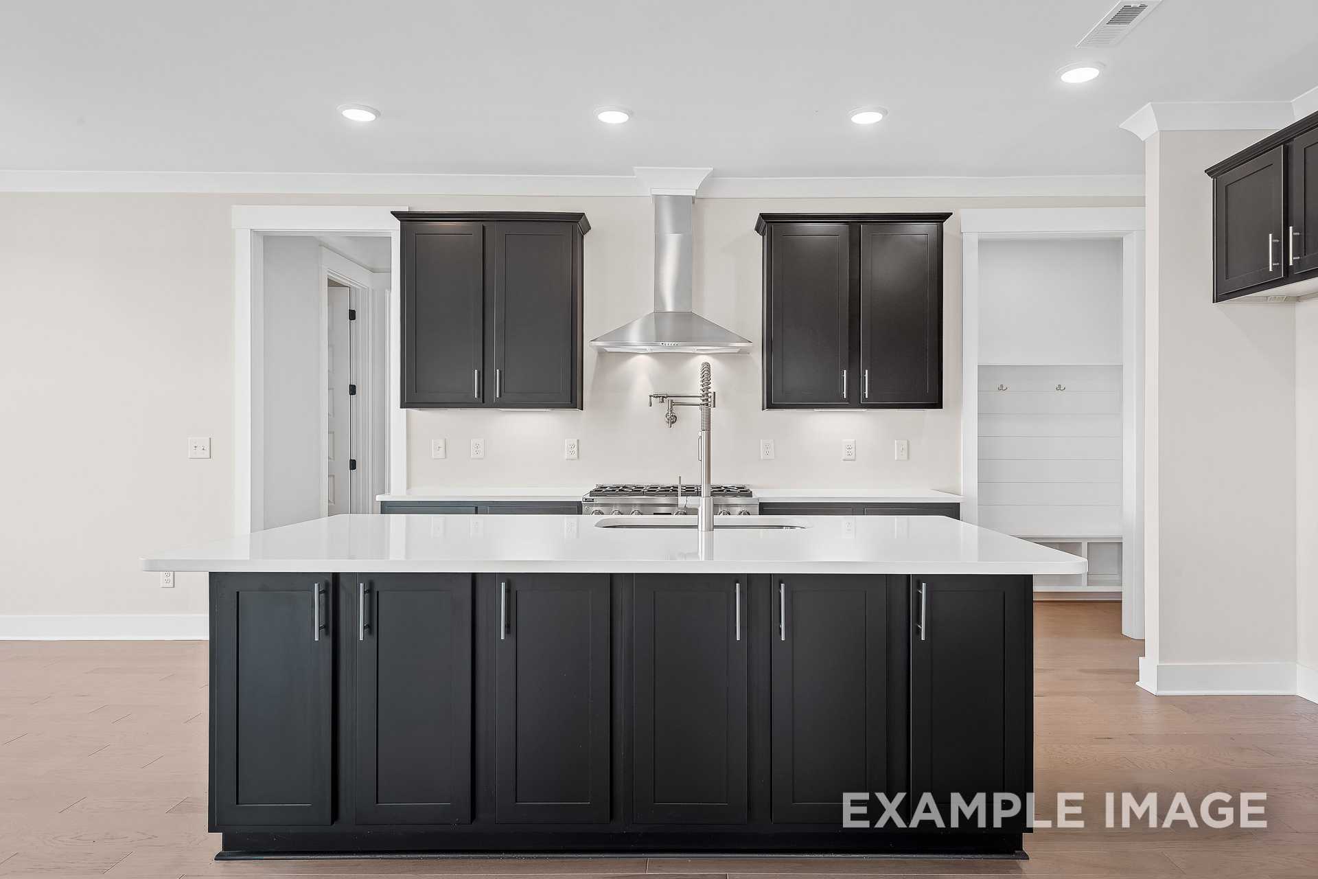 Modern kitchen in The Hawkins featuring large white island, black shaker cabinets, gas range, and stainless hood