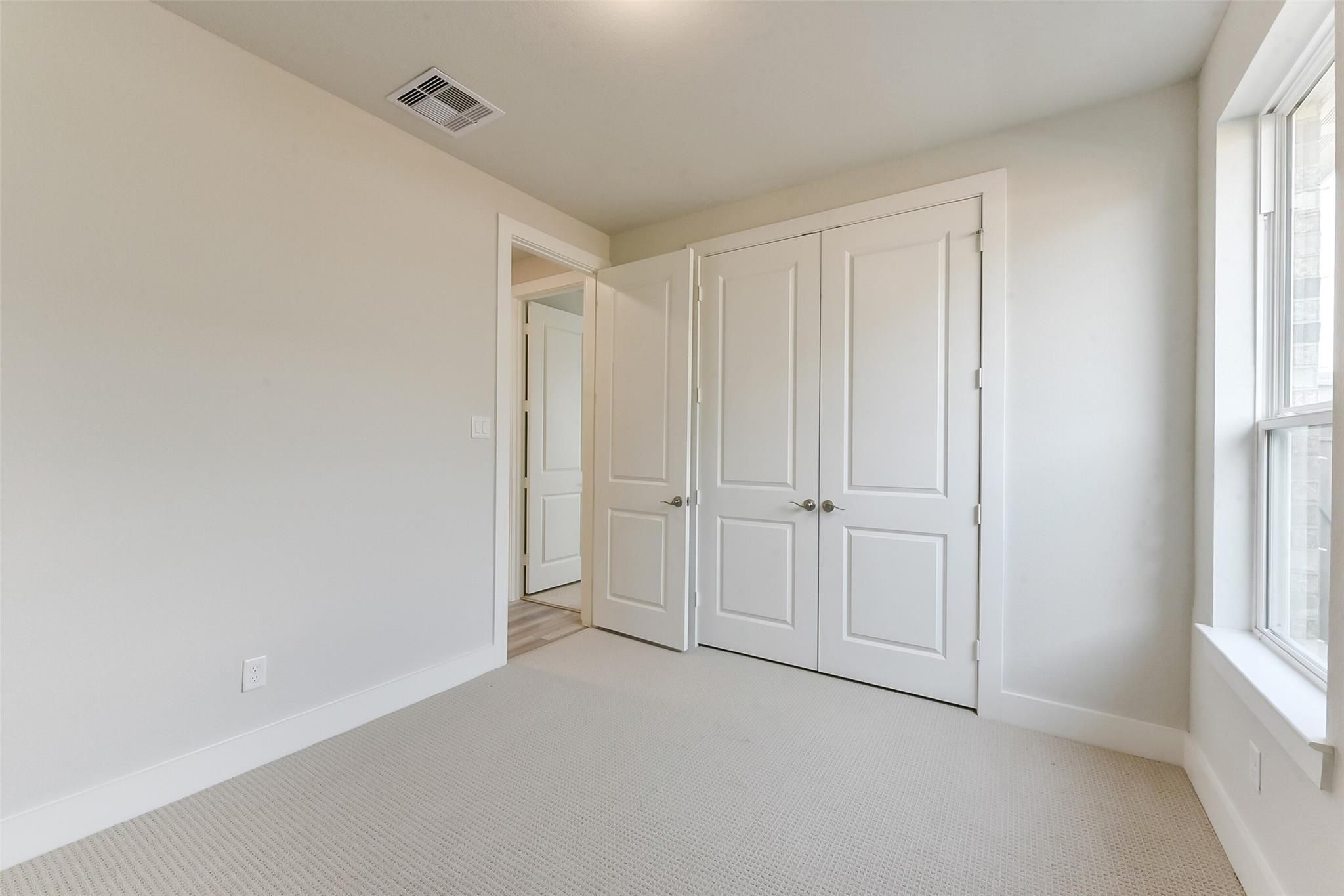 Bright secondary bedroom with double-door closet, beige walls, and large window in Davidson Homes The Edward A, Lago Mar, Texas City
