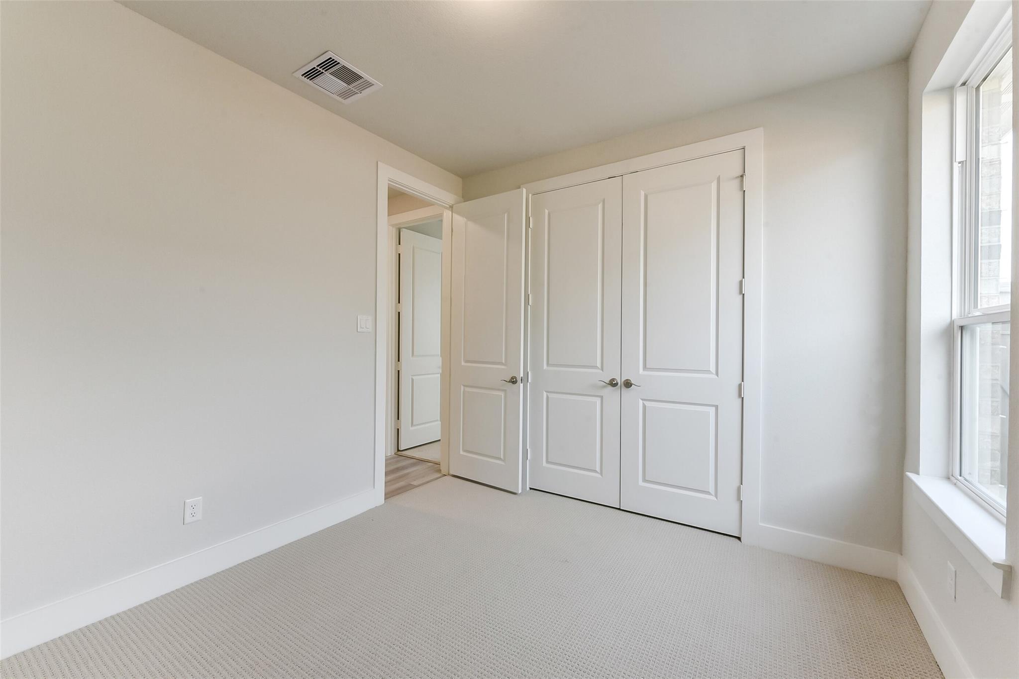 Bright secondary bedroom with double-door closet, beige walls, and large window in Davidson Homes The Edward A, Lago Mar, Texas City