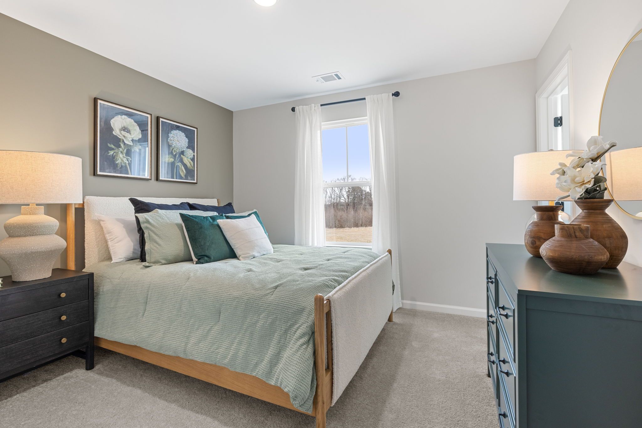Cozy bedroom at Links Crossing in Auburn Alabama with upholstered bed, teal pillows, gray walls, floral art, and window view
